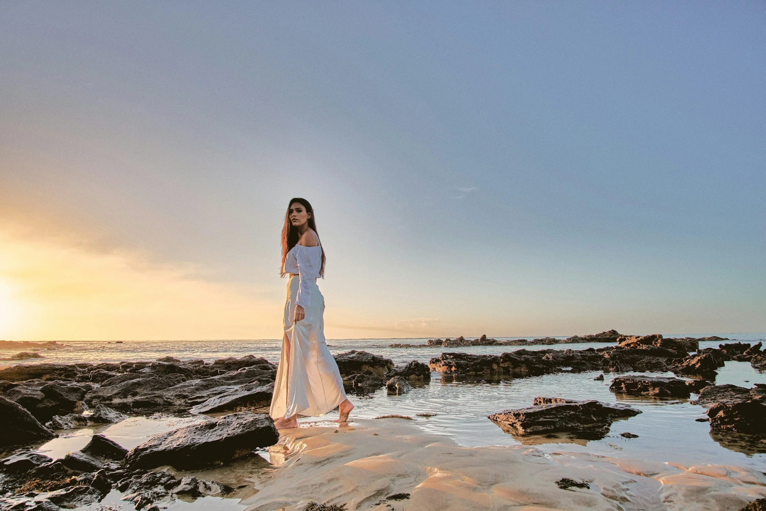 Woman standing by the ocean at sunset, representing holistic counseling, connecting to emotional healing, and somatic healing.