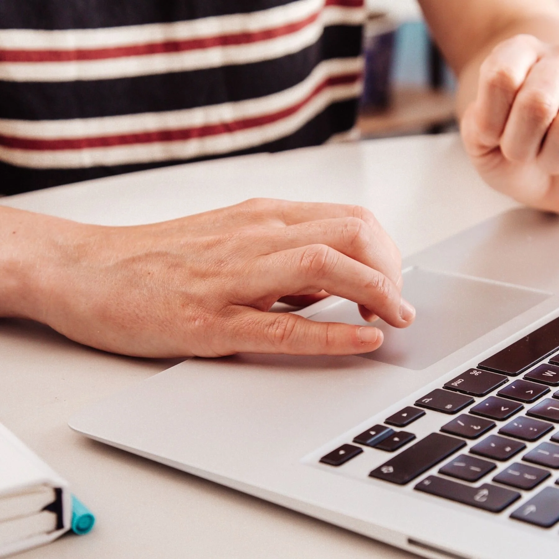 Person using a laptop touchpad on a desk with notebooks nearby.
