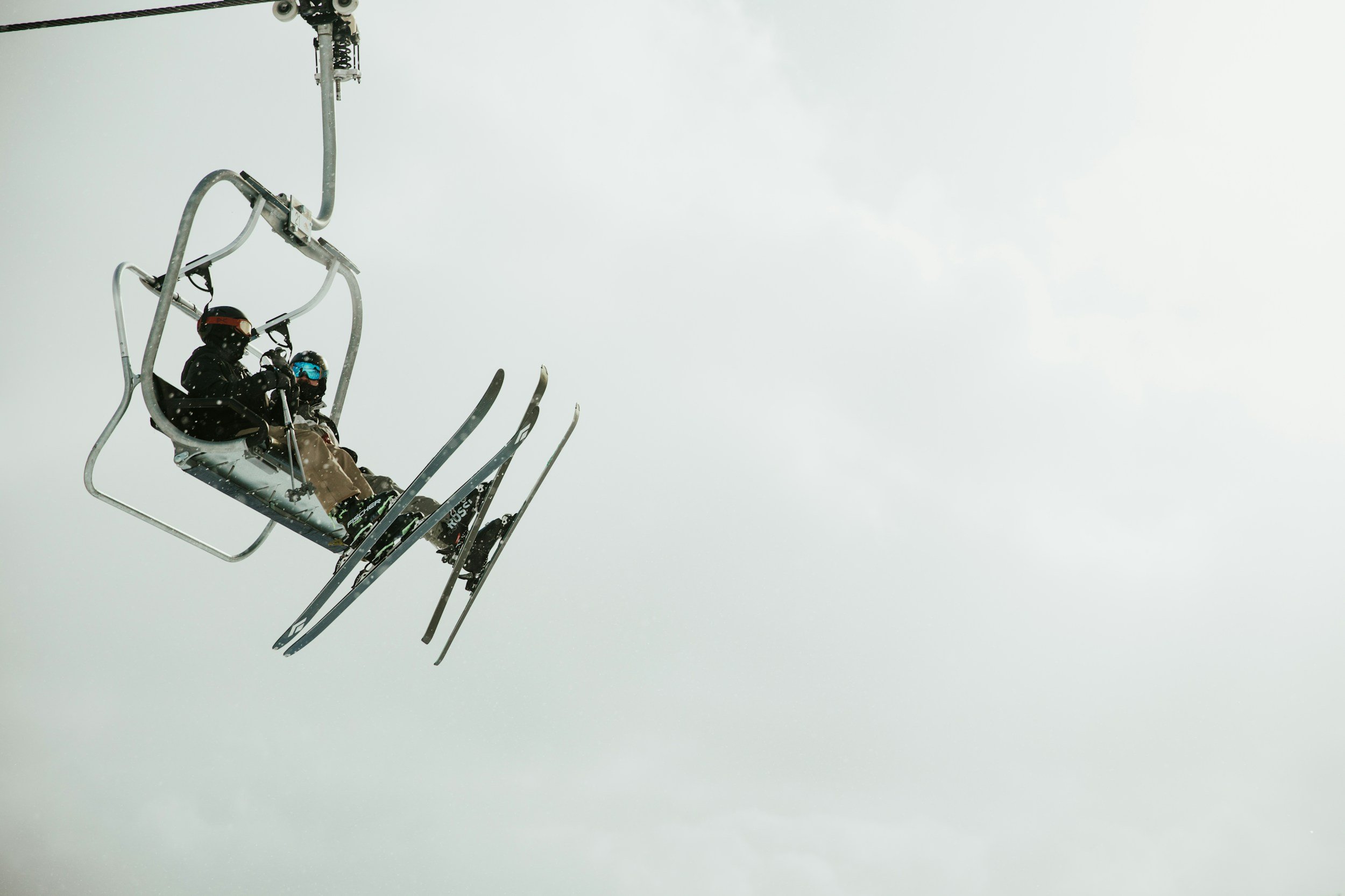Two skiers on a chairlift against a cloudy sky.