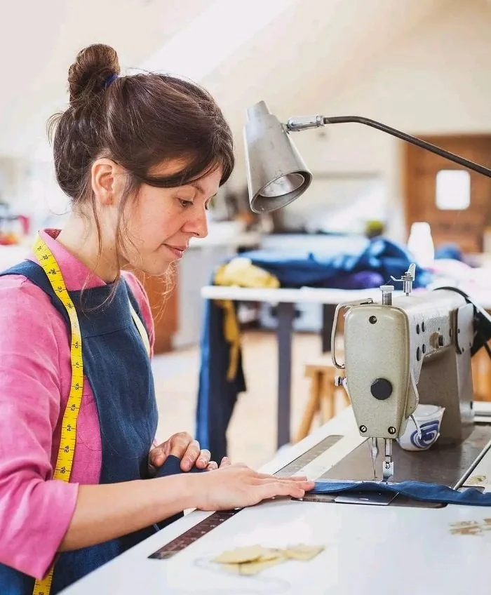 Woman sewing with industrial sewing machine, wearing apron and measuring tape