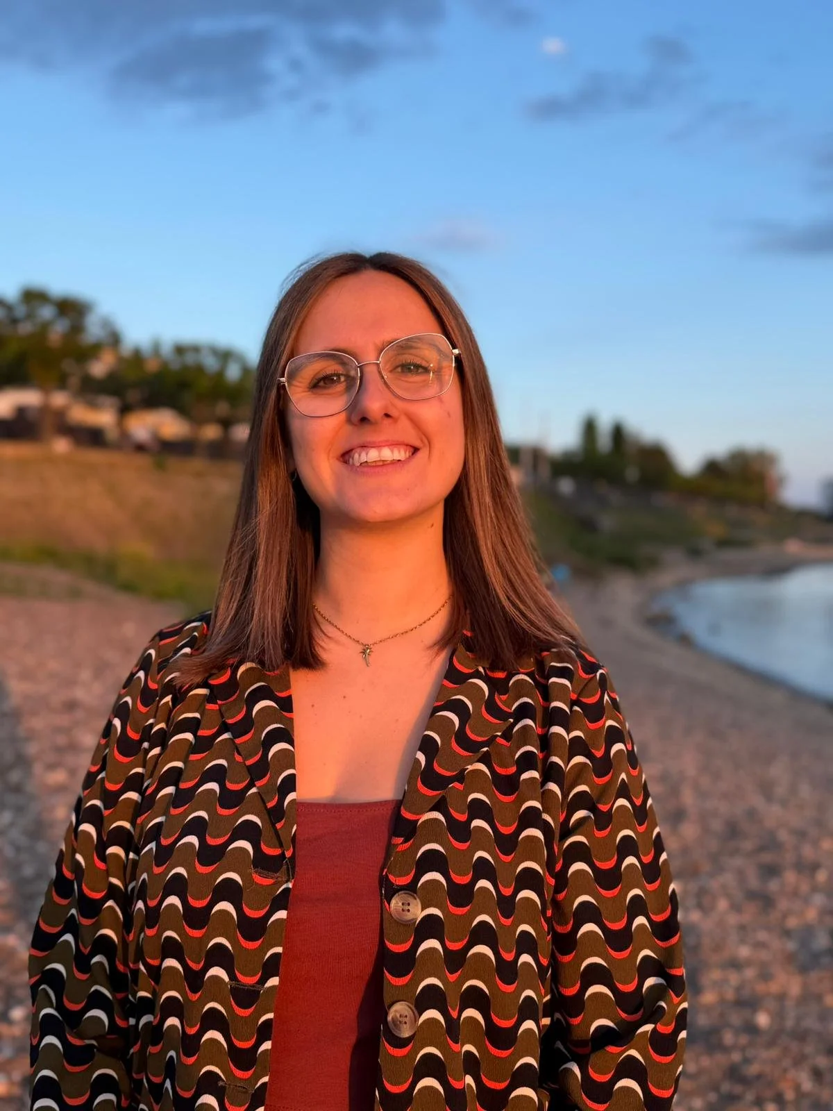 Junge Frau mit Brille steht am Strand bei Sonnenuntergang.