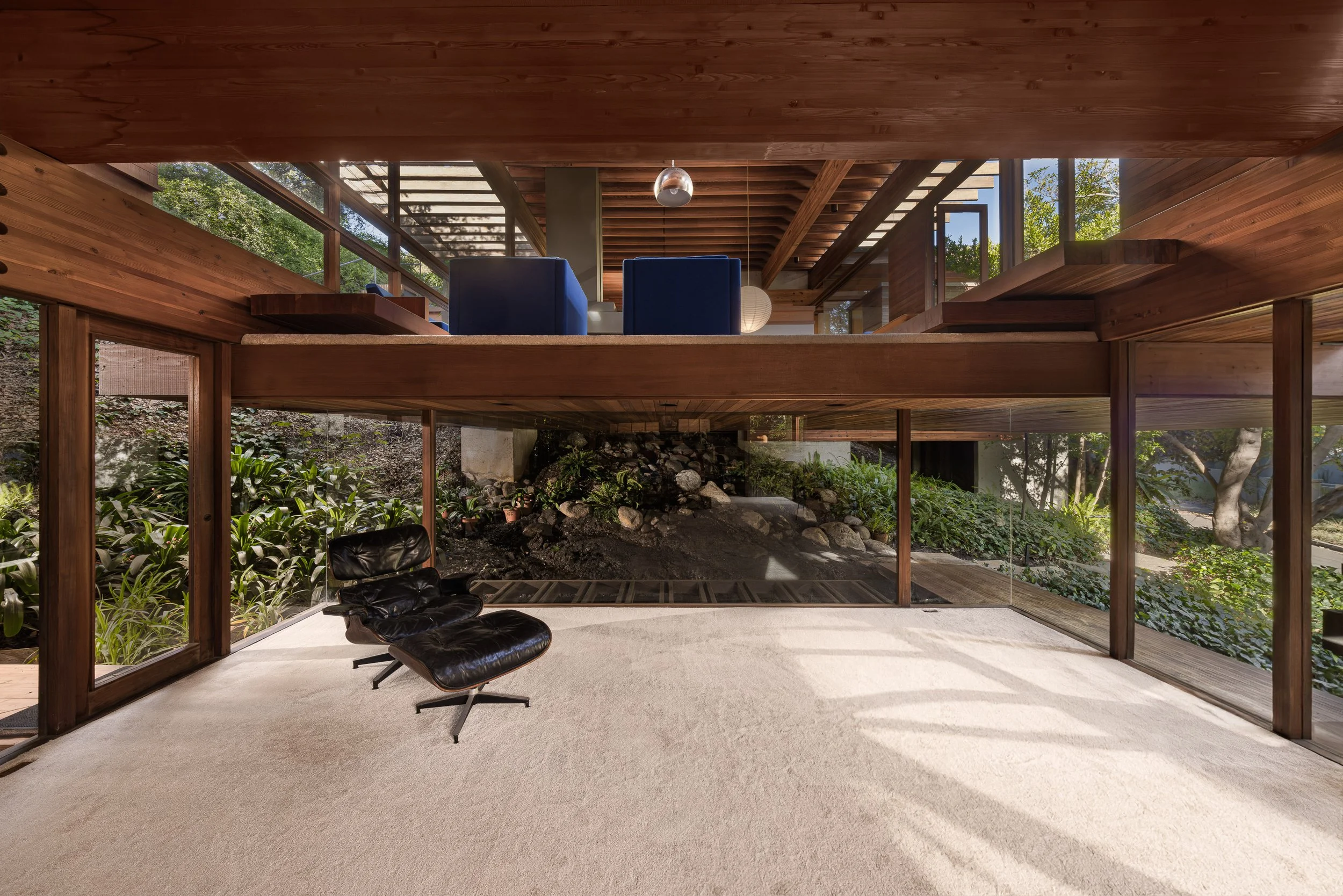 modern house interior with large windows, wooden beams, and a black leather lounge chair on a beige carpet.