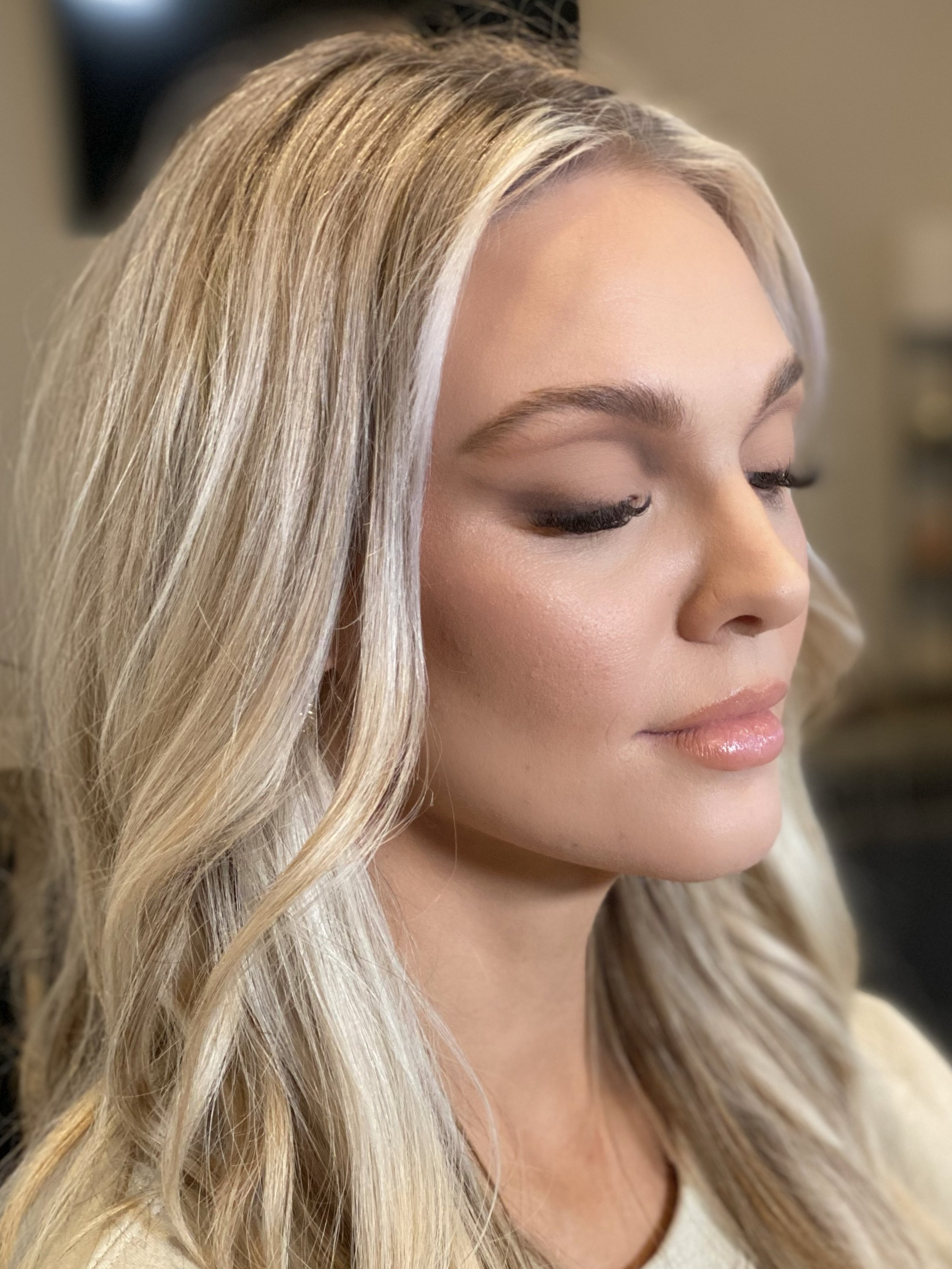 Close-up of a woman with platinum blonde hair styled in loose waves, with her eyes closed and a neutral expression.