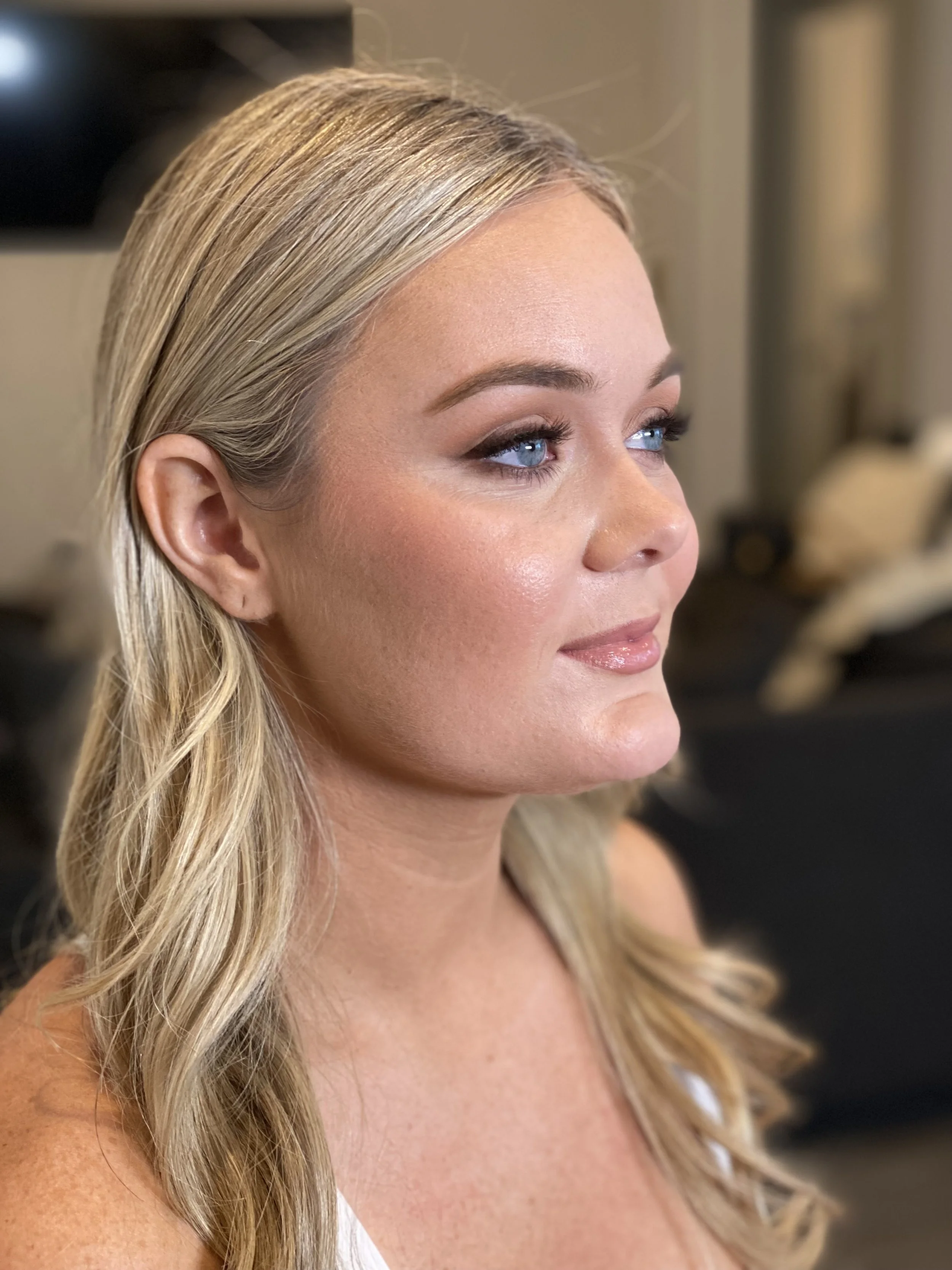 A close-up profile of a woman with blonde hair and blue eyes, wearing makeup with natural tones, looking slightly upwards.