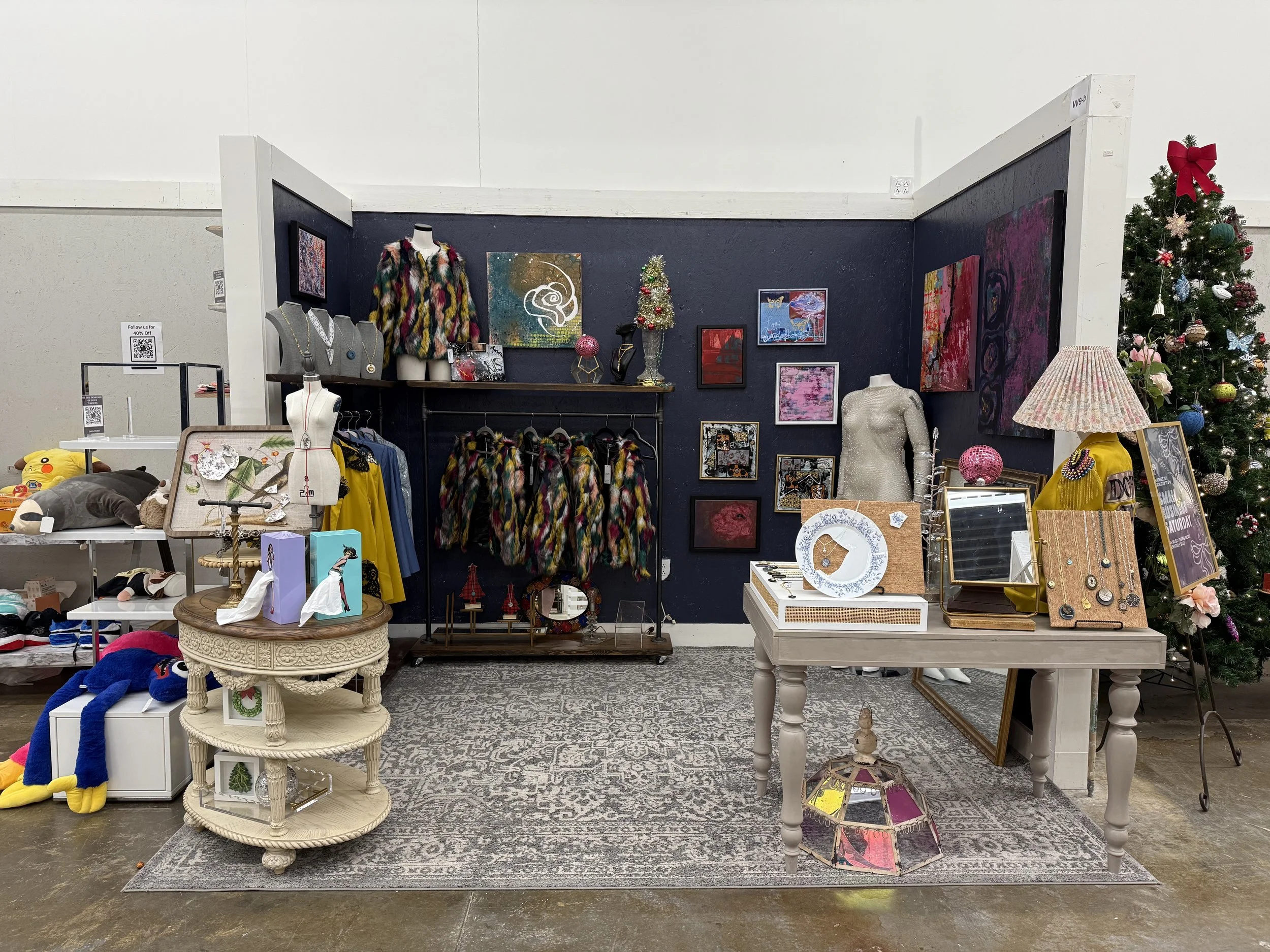 A display of clothing, jewelry, and art in a store with a decorated Christmas tree on the right side.