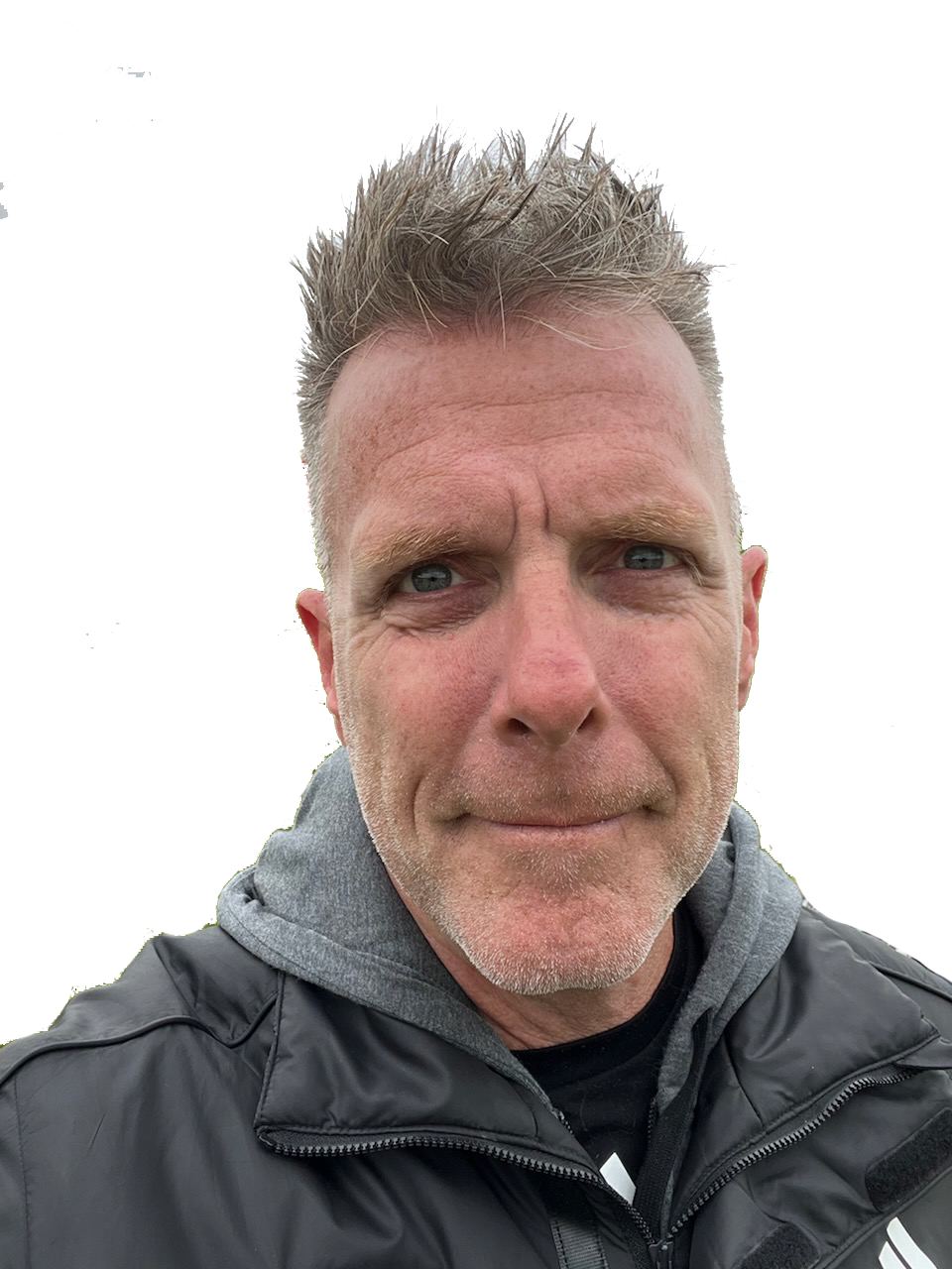 A man with short, spiked, gray hair and light skin, wearing a gray hoodie under a black jacket, taking a selfie outdoors.