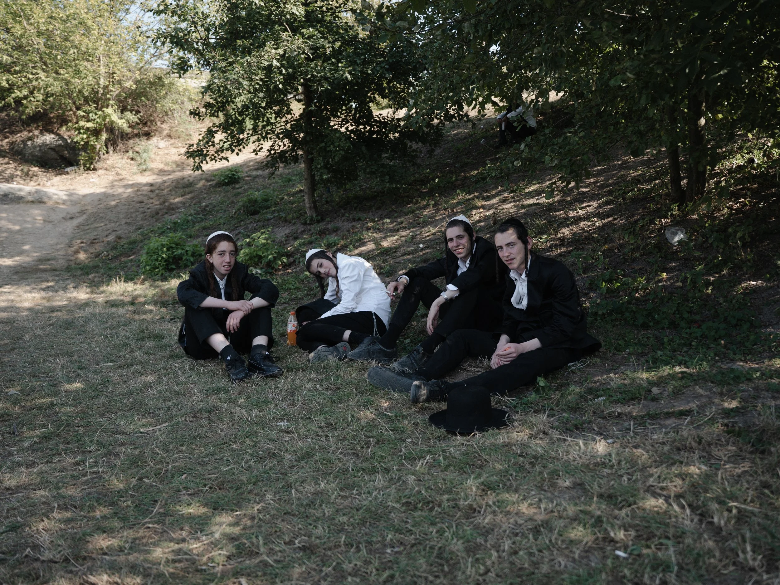 Four young people sitting on the grass under trees in a park, smiling and relaxing.