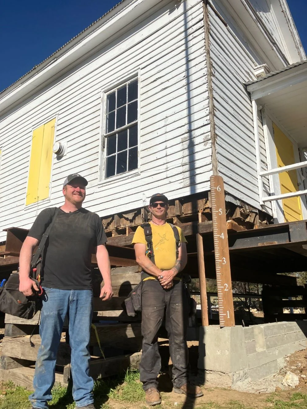 Two workers standing by the building corner with the oversized ruler showing the distance to lower.