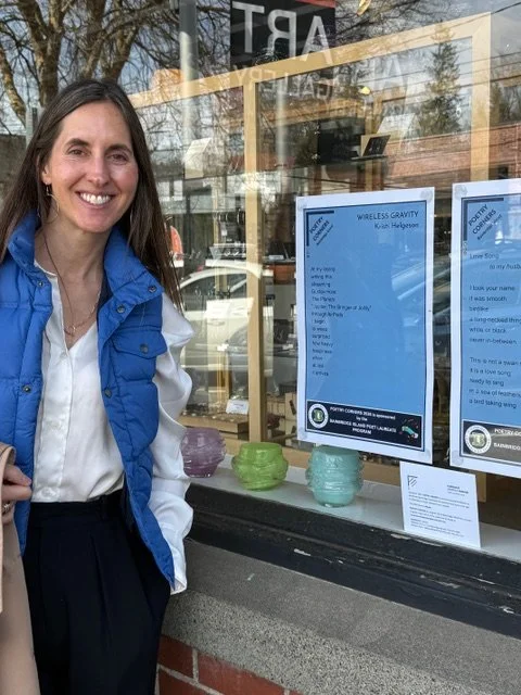 Kristi Helgeson stands in front of her poem in the window at Bainbridge Arts & Crafts in downtown Winslow. During April select poems are displayed in storefront windows in recognition of National Poetry Month!
.
Kristi is one of many locals who submi