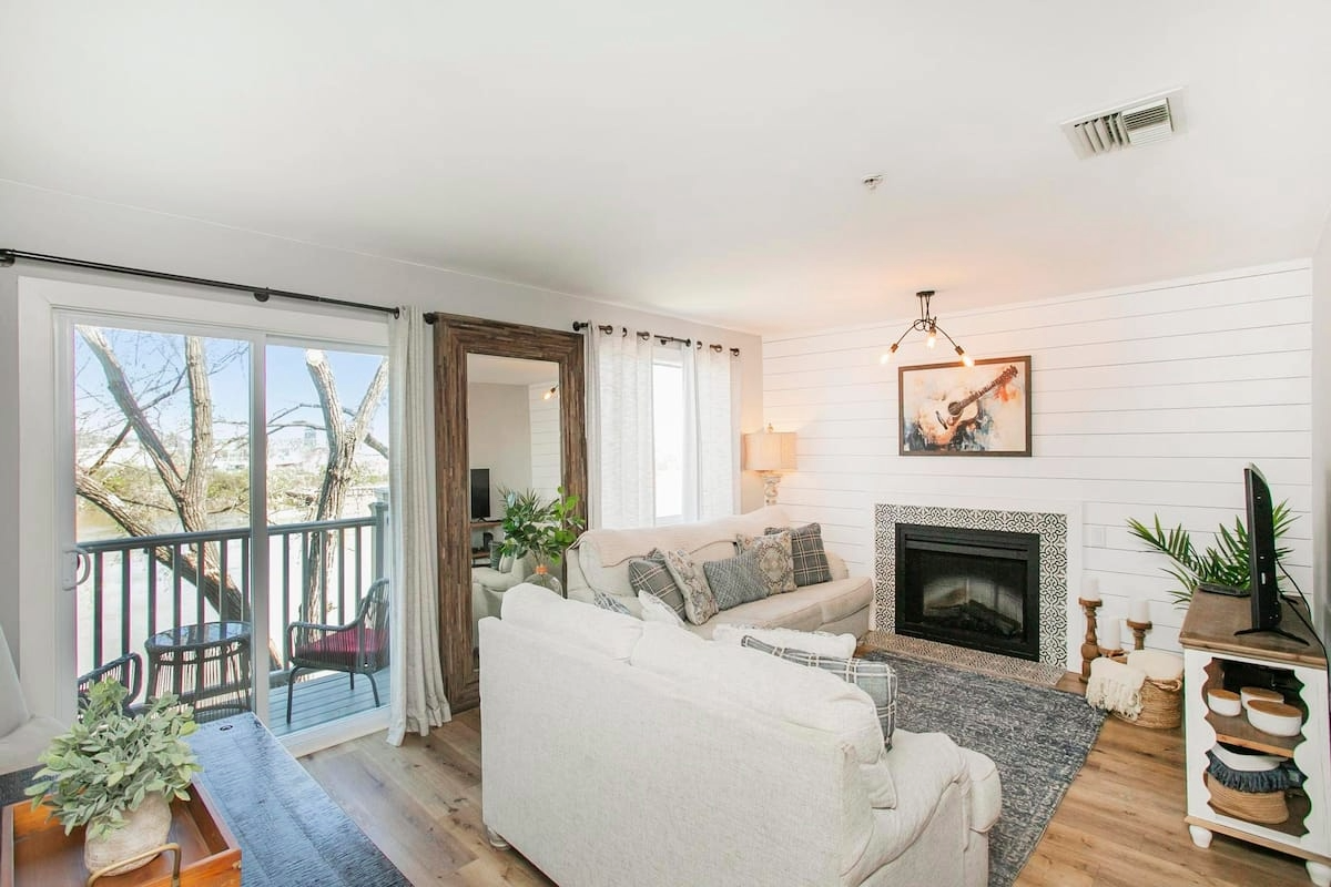 Cozy downtown Nashville condo living room with fireplace, mounted TV, and modern furnishings, plus views of the pool, balcony, and bedrooms.