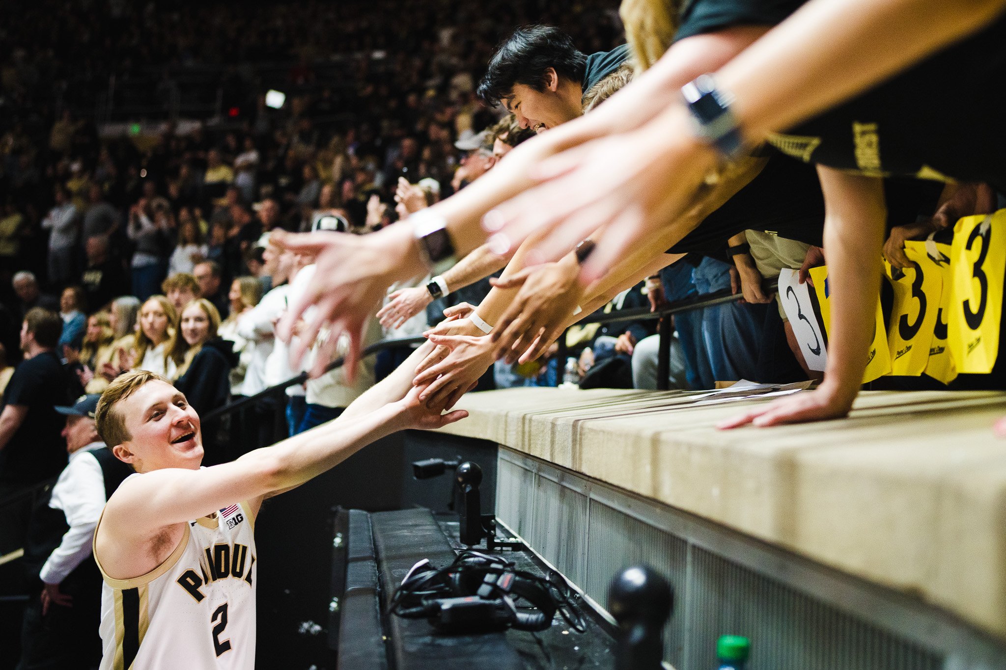 A cheerleader reaching out to shake hands with a player at a basketball game, with a crowd in the background.