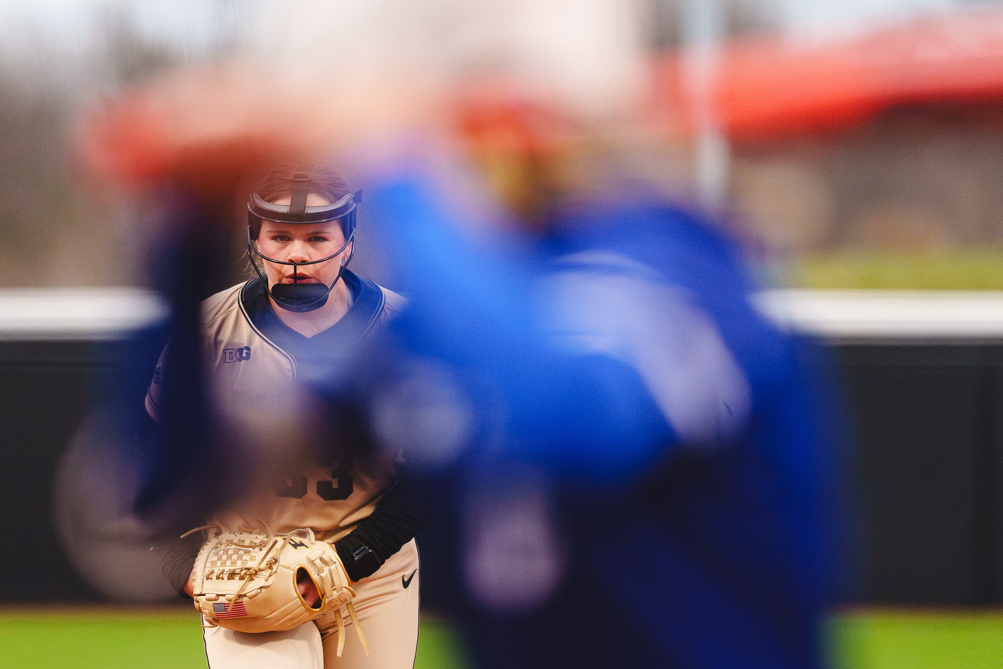 A female softball player in uniform with a glove and helmet, focused during a game.