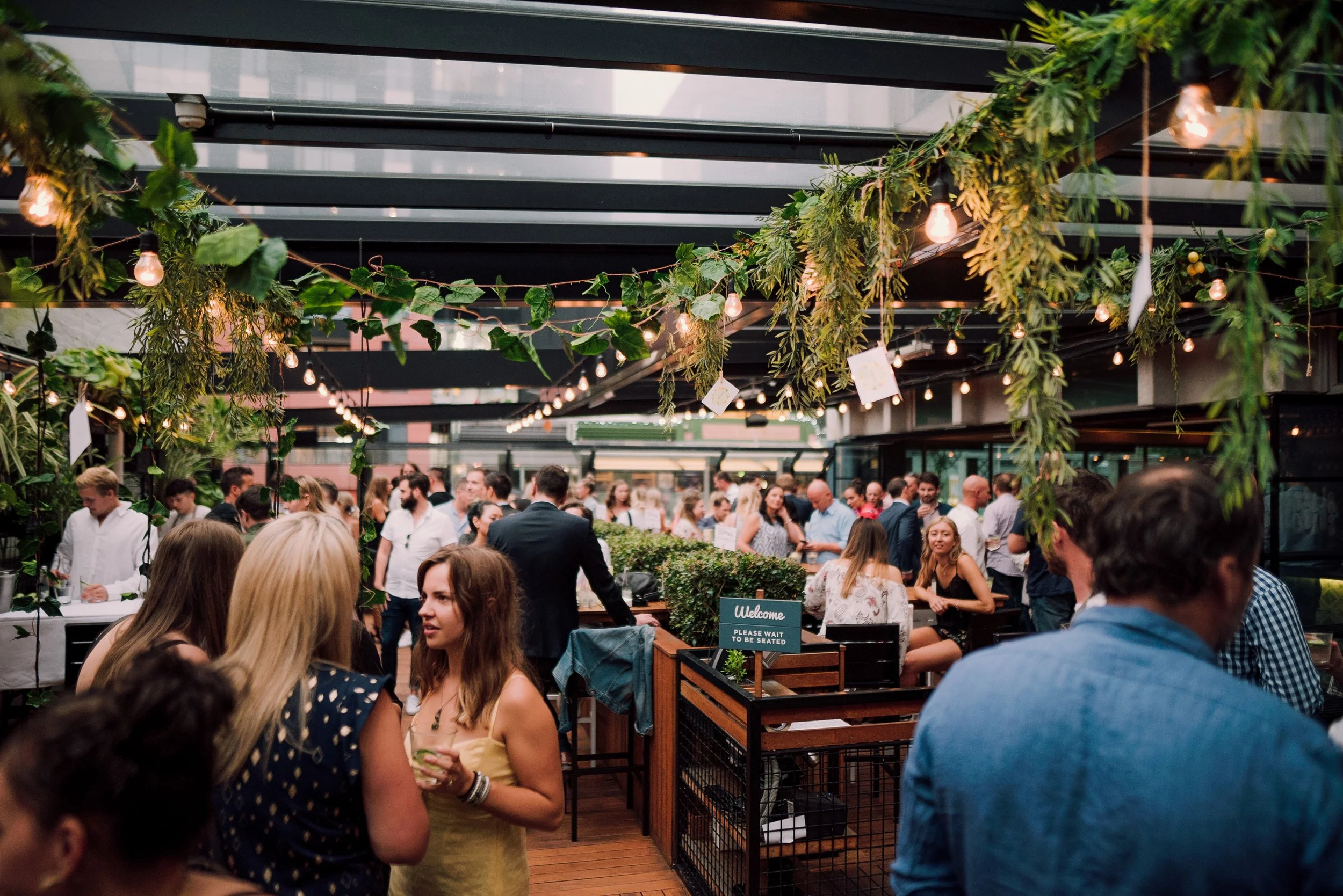 Guests socialising with drinks under greenery and festoon lights on the Glass Goose deck