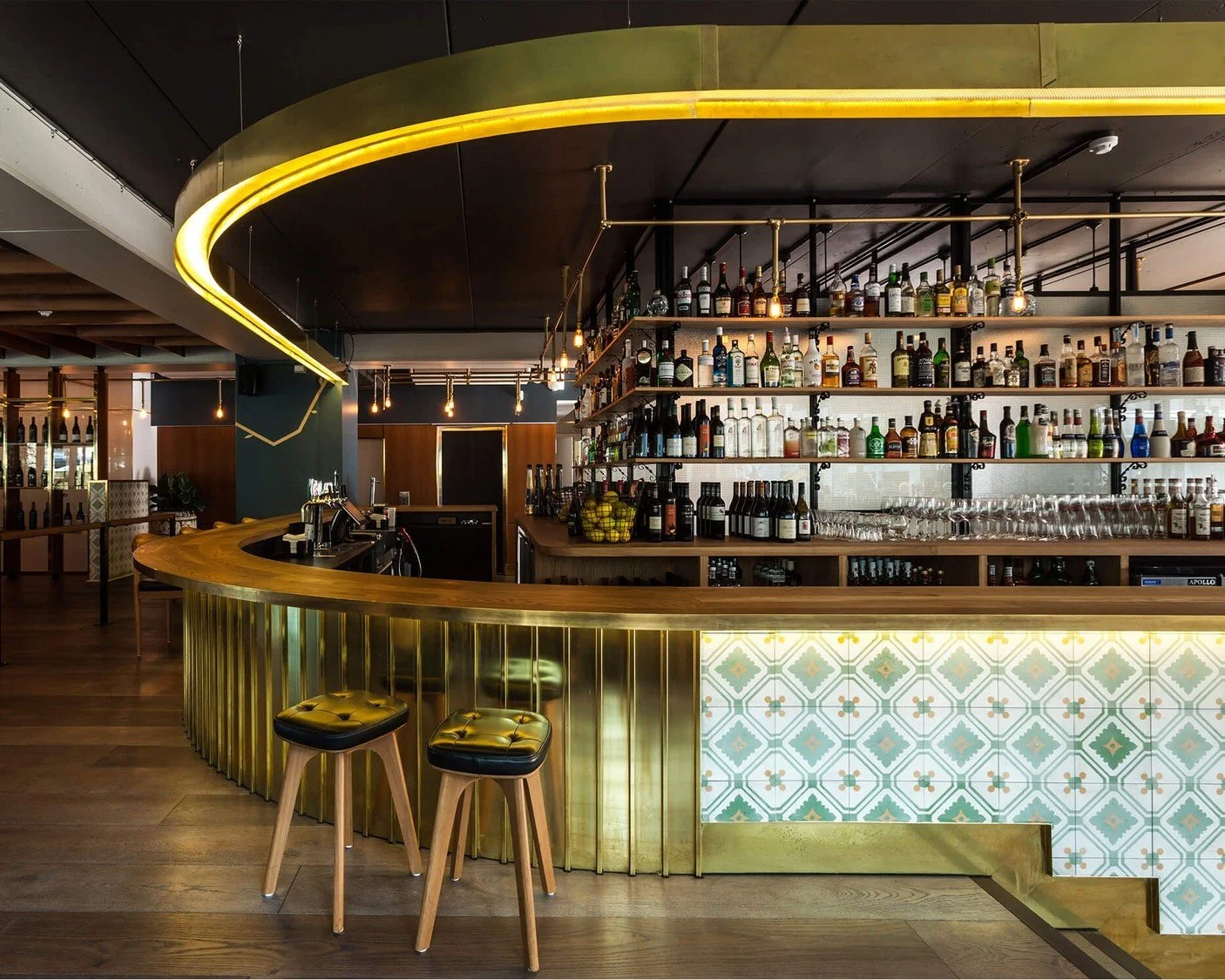 Curved brass bar with a gold halo light and patterned tiles in an exclusive-hire space