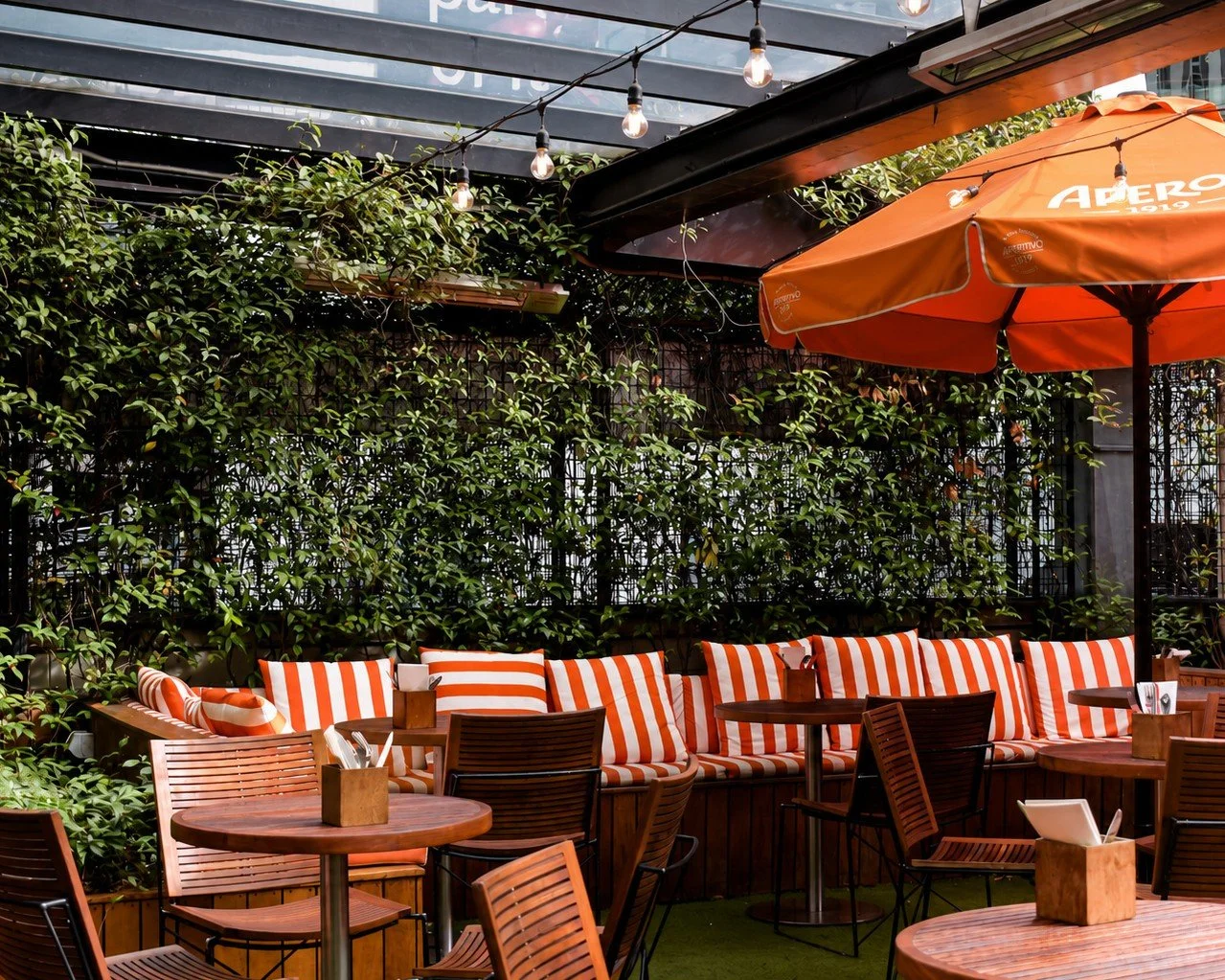 Outdoor terrace seating with striped cushions and climbing greenery under festoon lights