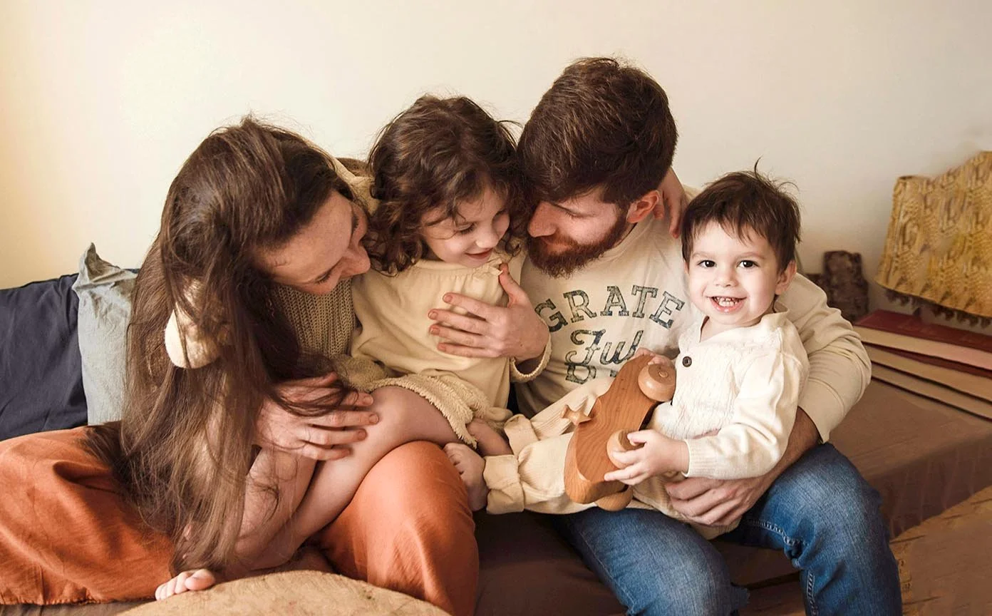 expat family with two kids sitting on couch together holding each other close and smiling