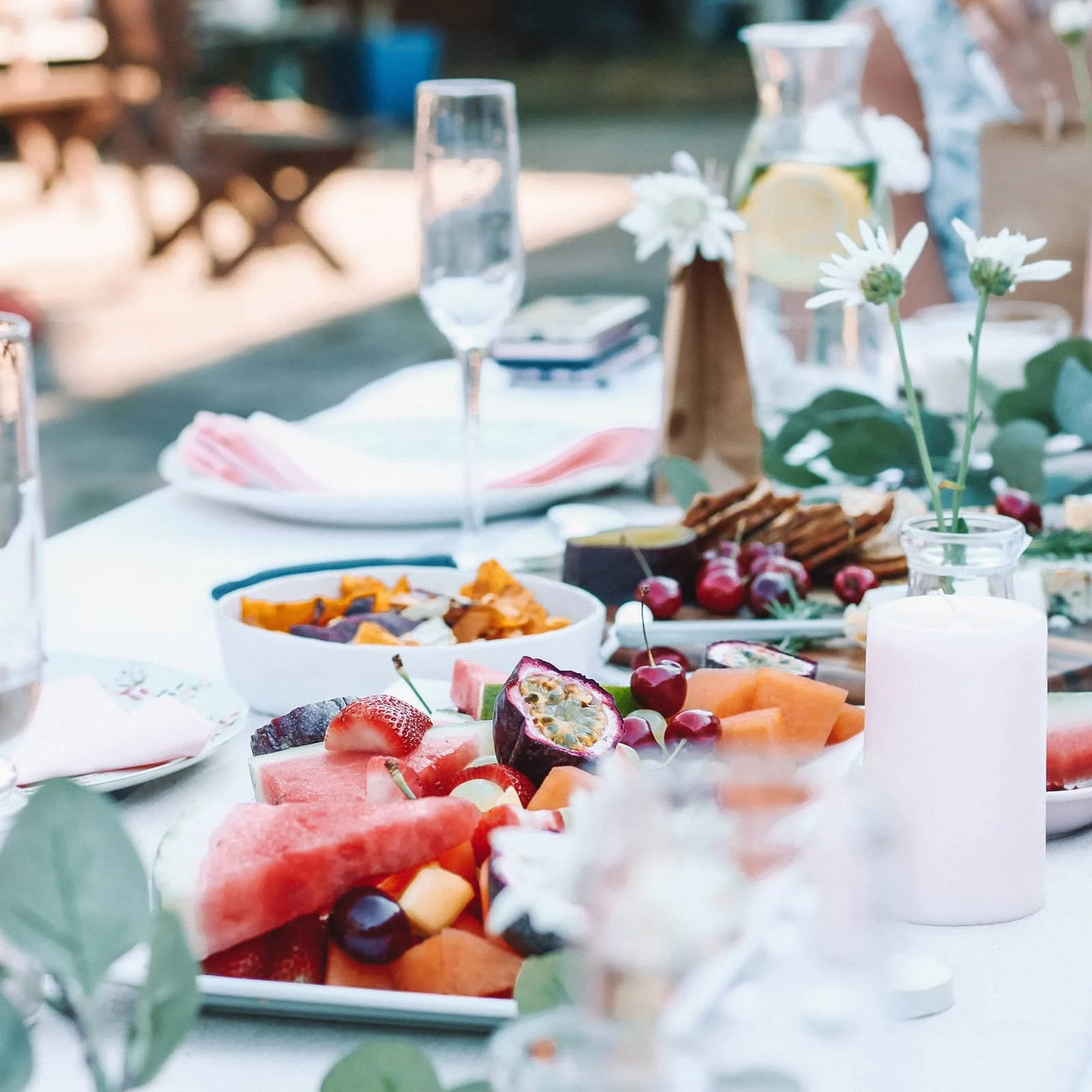 A plate of fruit and cheese on a summery outside table