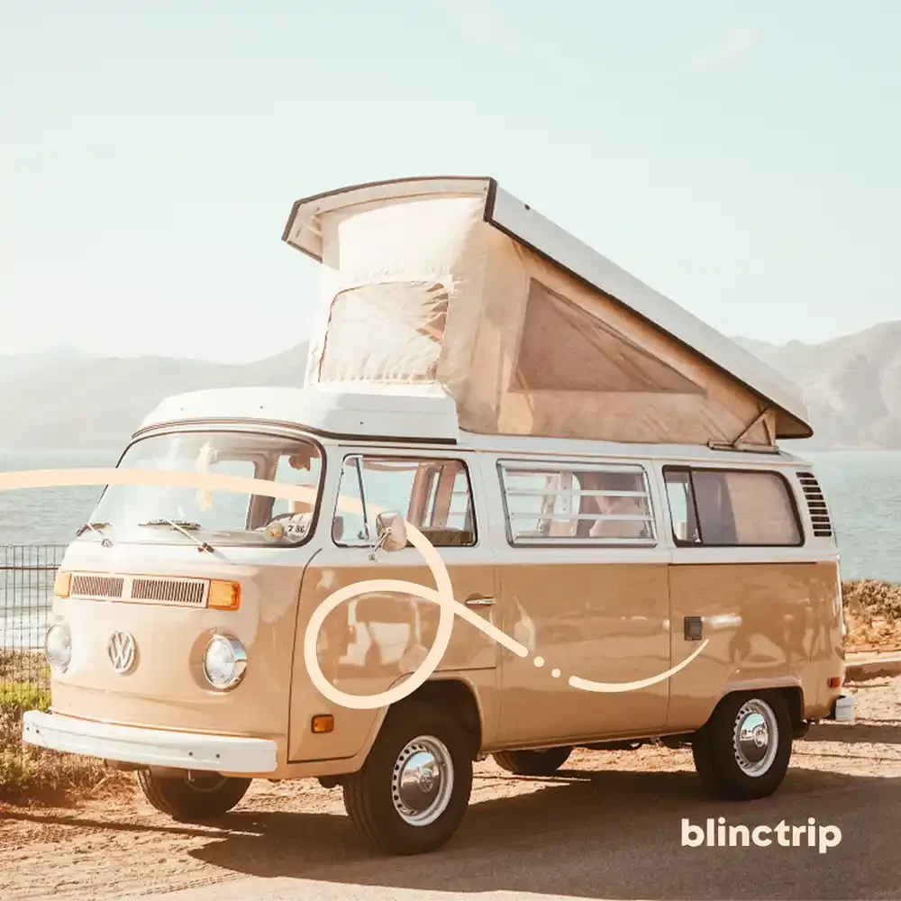 A vintage Volkswagen camper van with a pop-up roof parked near a body of water with mountains in the background.