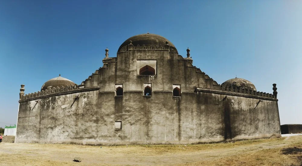 Historic fortress or mosque with domes and high walls under a clear blue sky.
