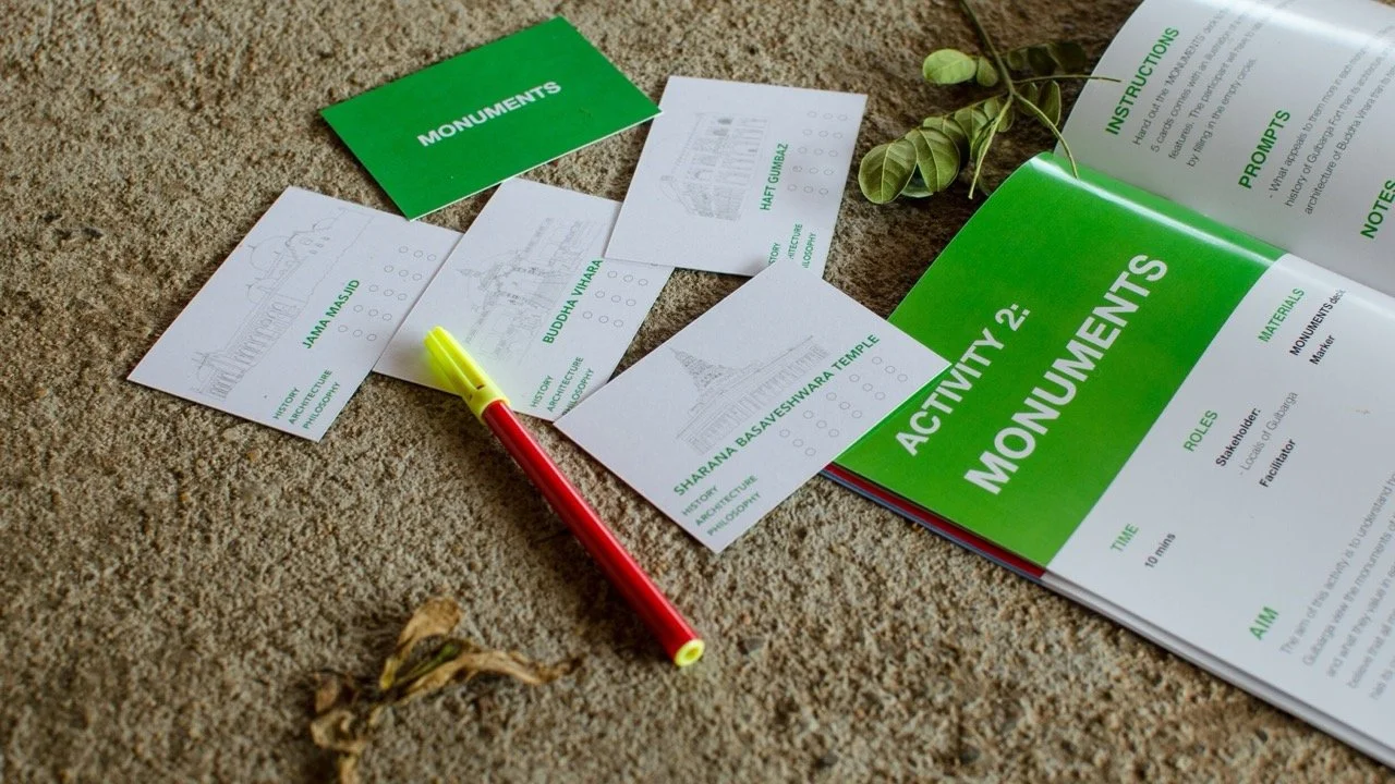 Activity book titled 'Monuments' with printed pages, a green pen, and sketch cards of different monuments on a carpet.