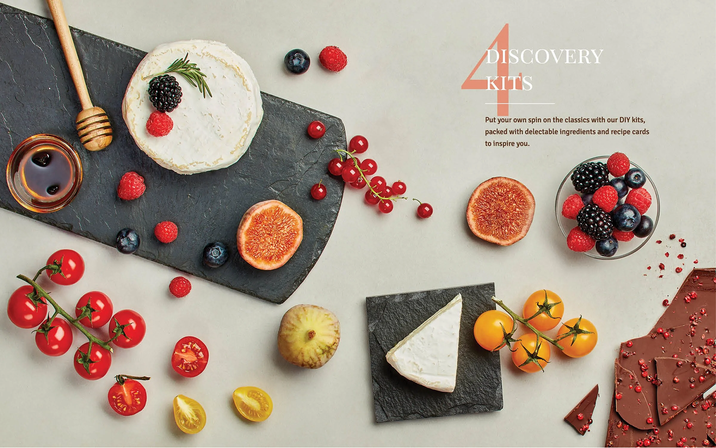 Flat lay of cheese, fresh berries, tomatoes, figs, chocolate, honey, and herbs on a light surface, with a promotional overlay for a discovery kit.