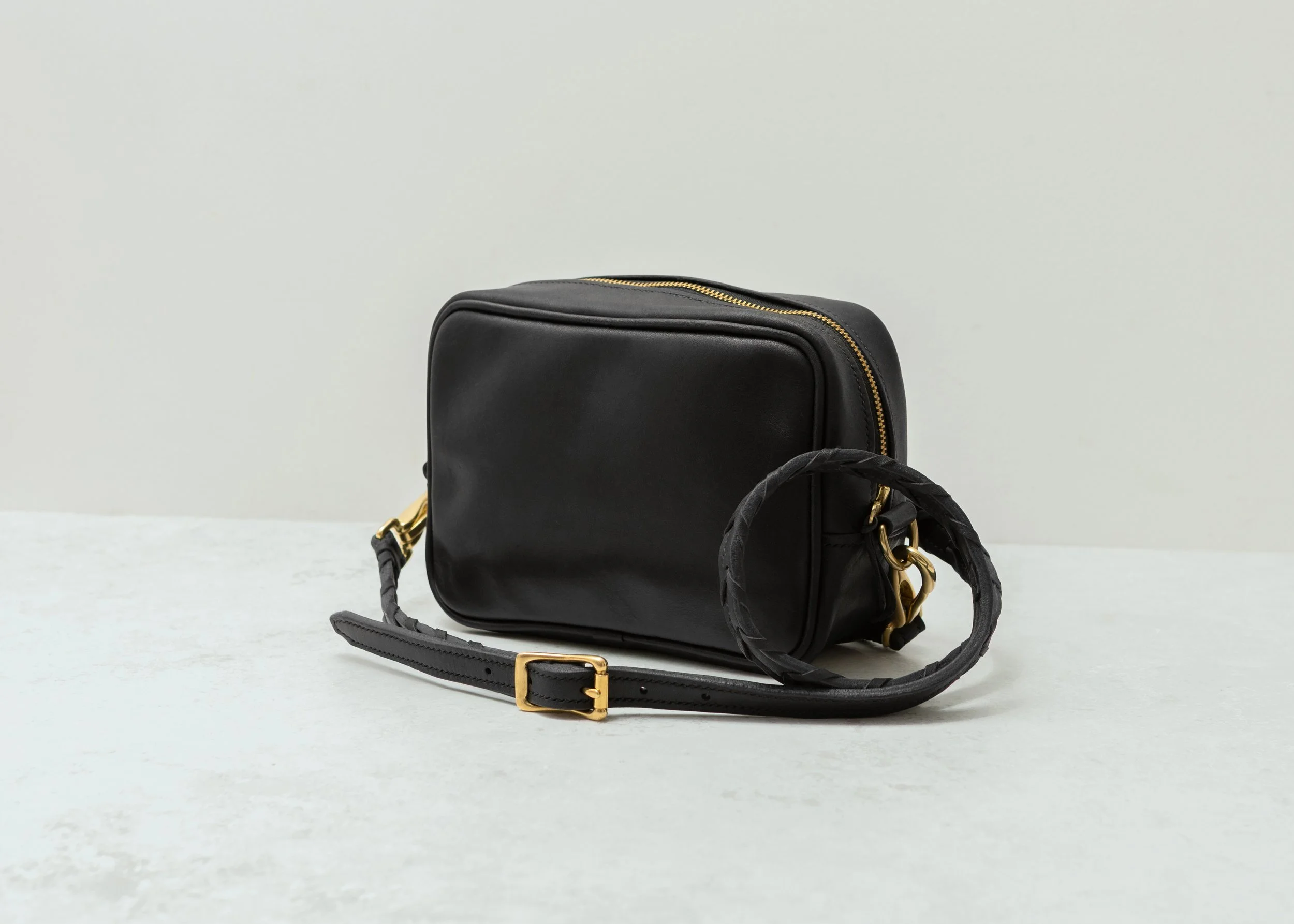 Black leather handbag with gold zippers and a detachable strap with gold hardware, placed on a light surface with a plain background.