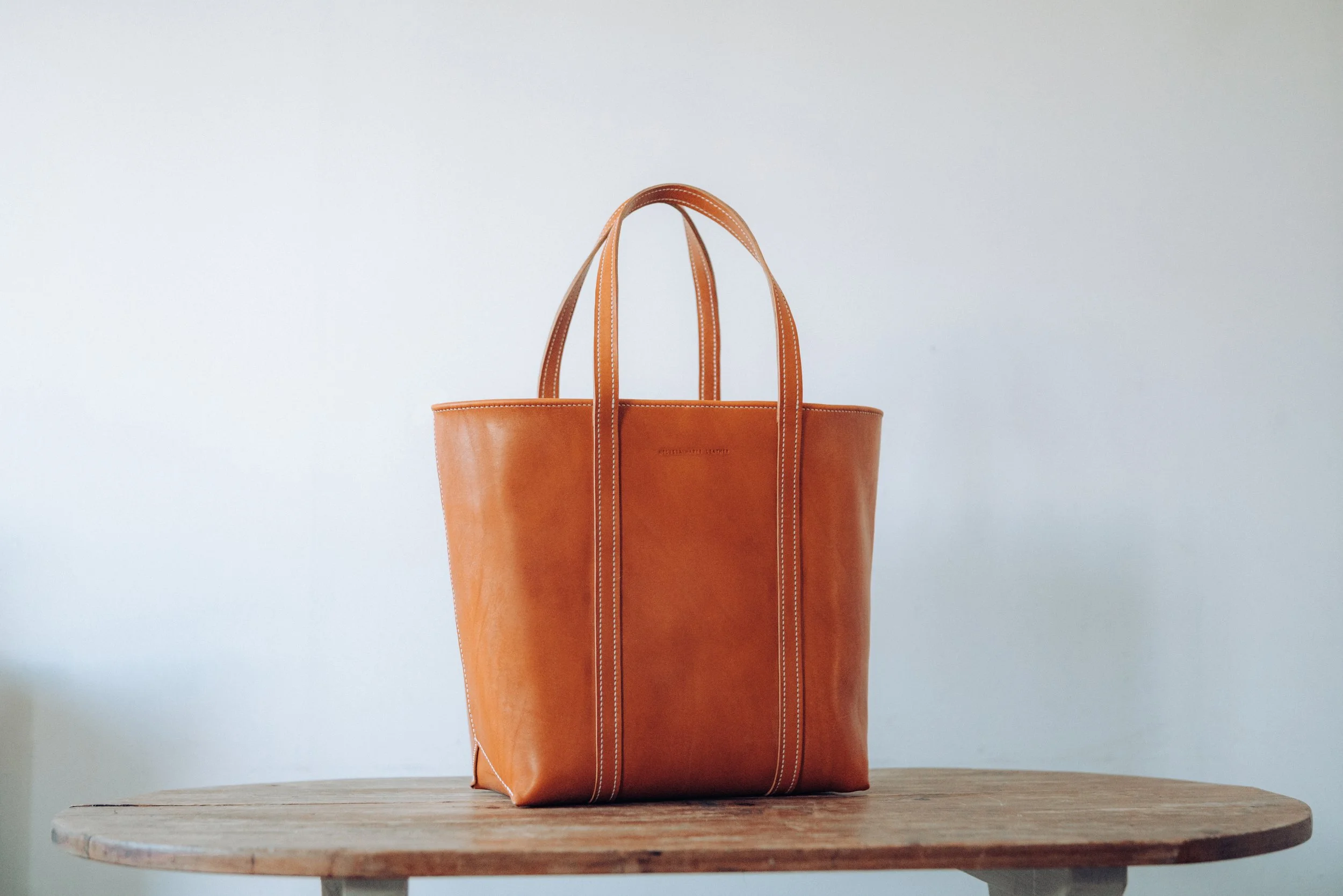 Brown leather tote bag on wooden table against white background.