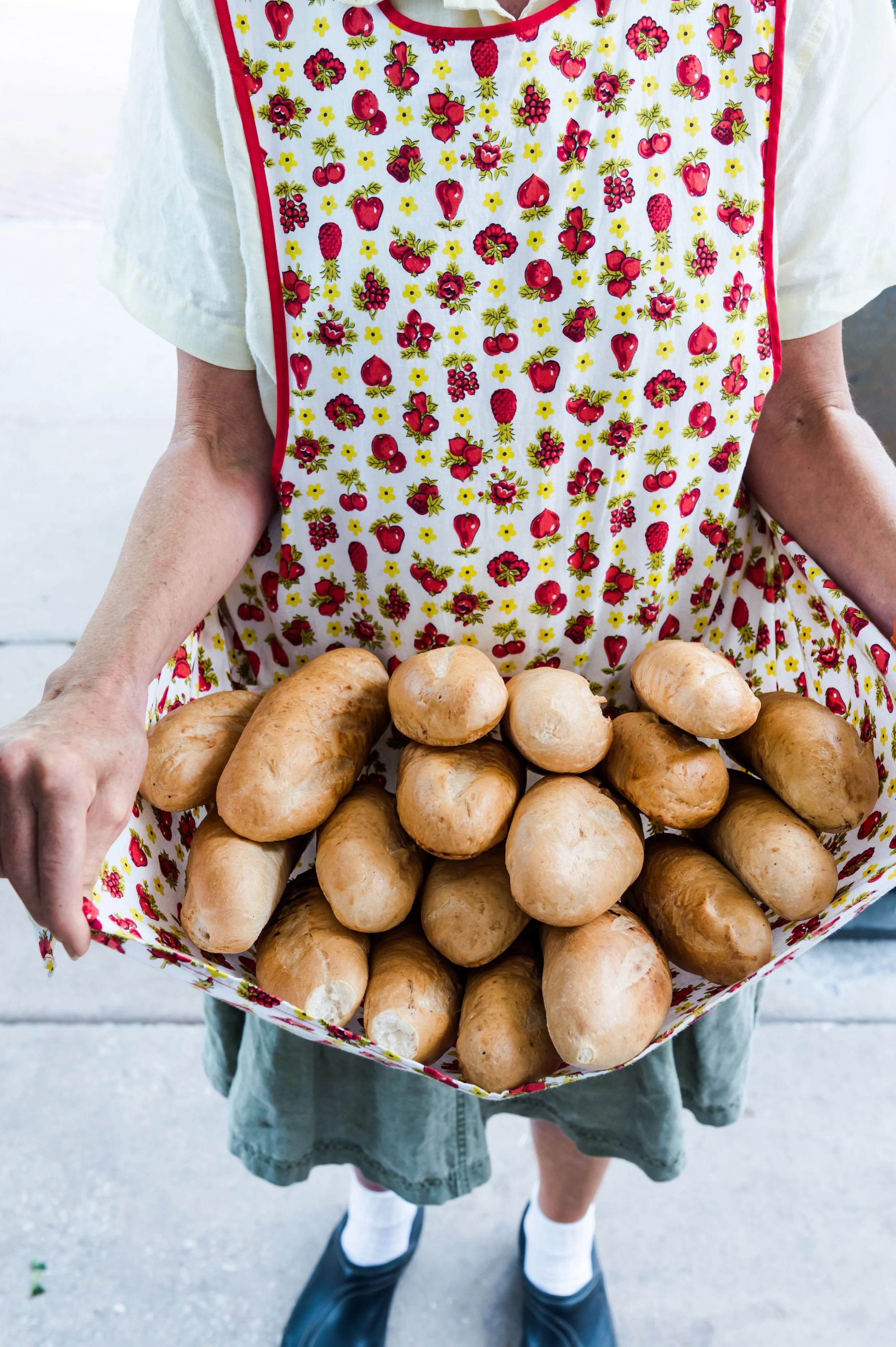 Person holding a bundle of bread in a floral apron outdoors.