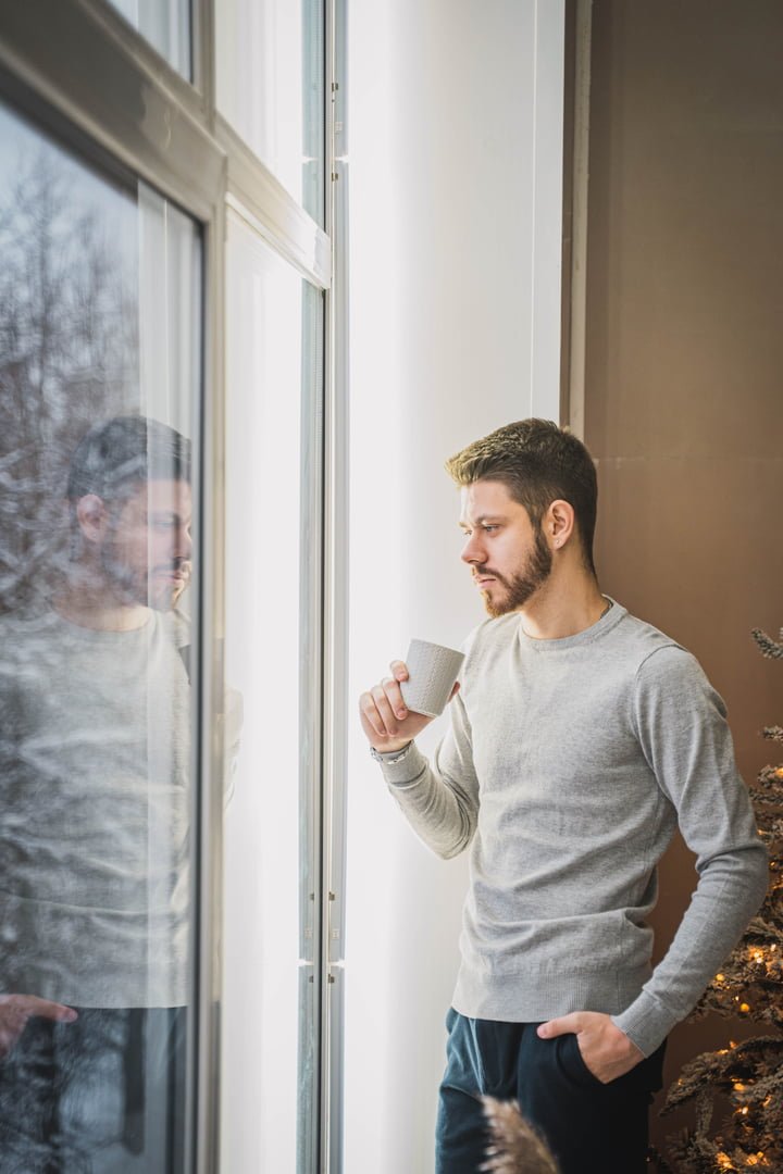 man looking out of his window with coffee
