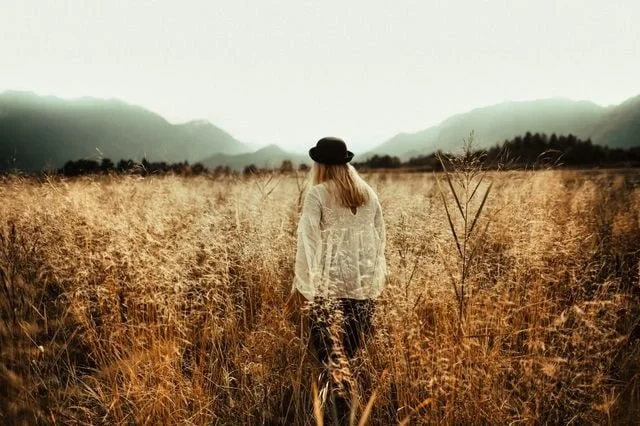 woman in white shirt and black hat walking through a field