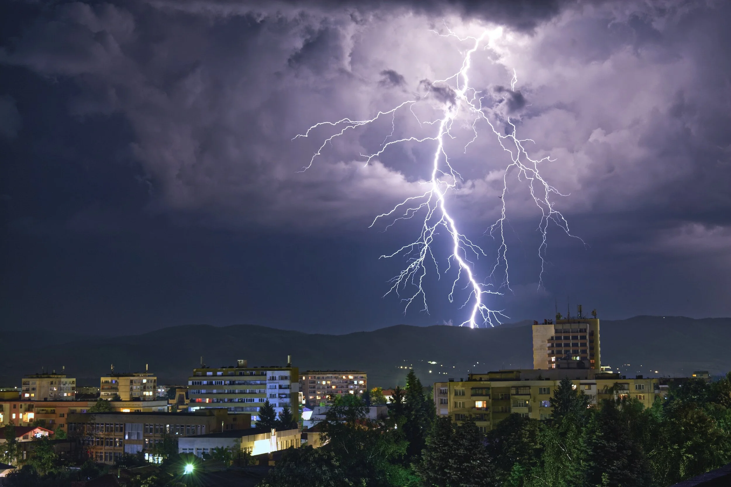 Dramatic lightning strike over urban skyline at night with dark clouds.