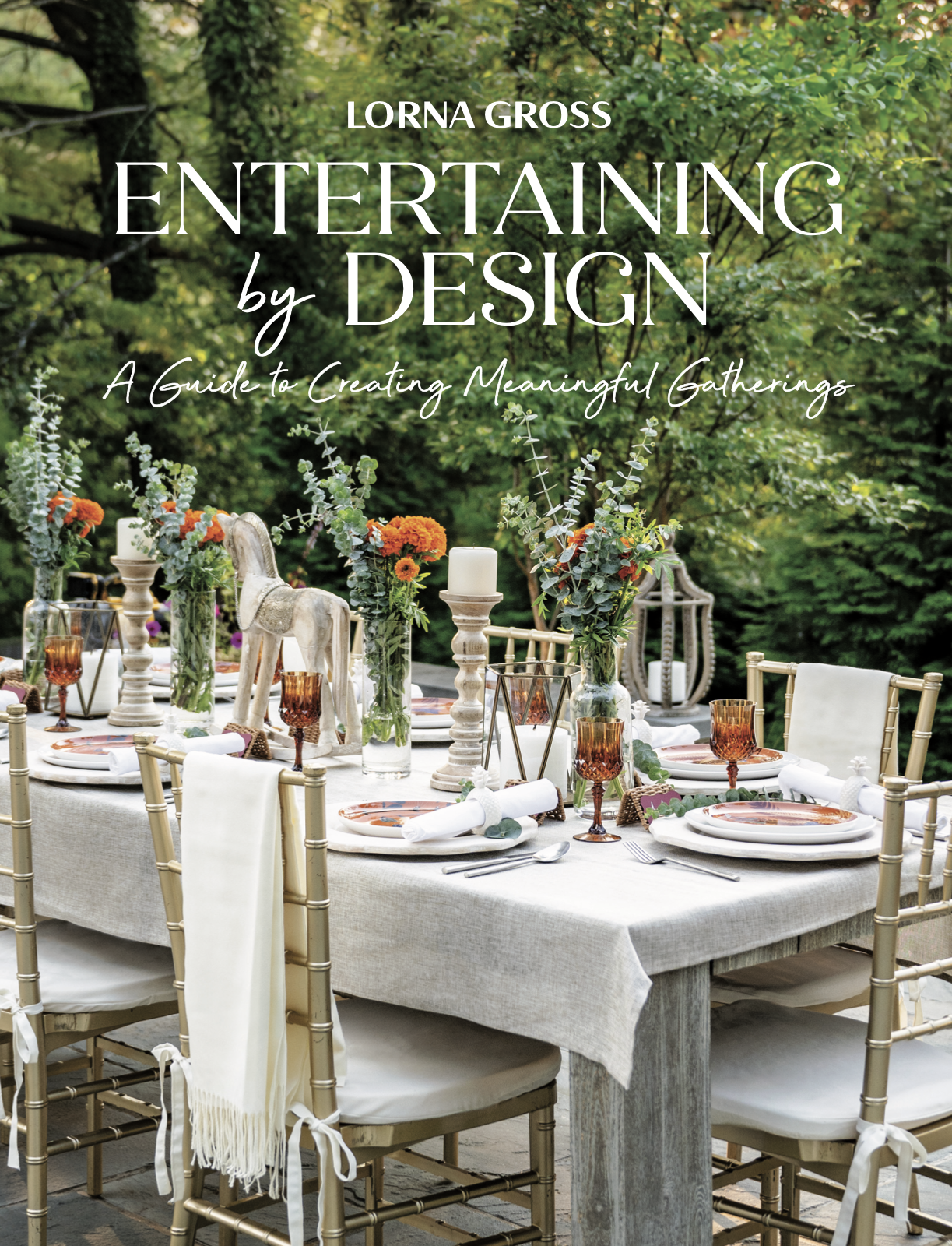 Cover of Lorna Gross tabletop book there is a Table set for an outdoor dinner with floral centerpieces, candles, plates, glasses, and cutlery surrounded by greenery.