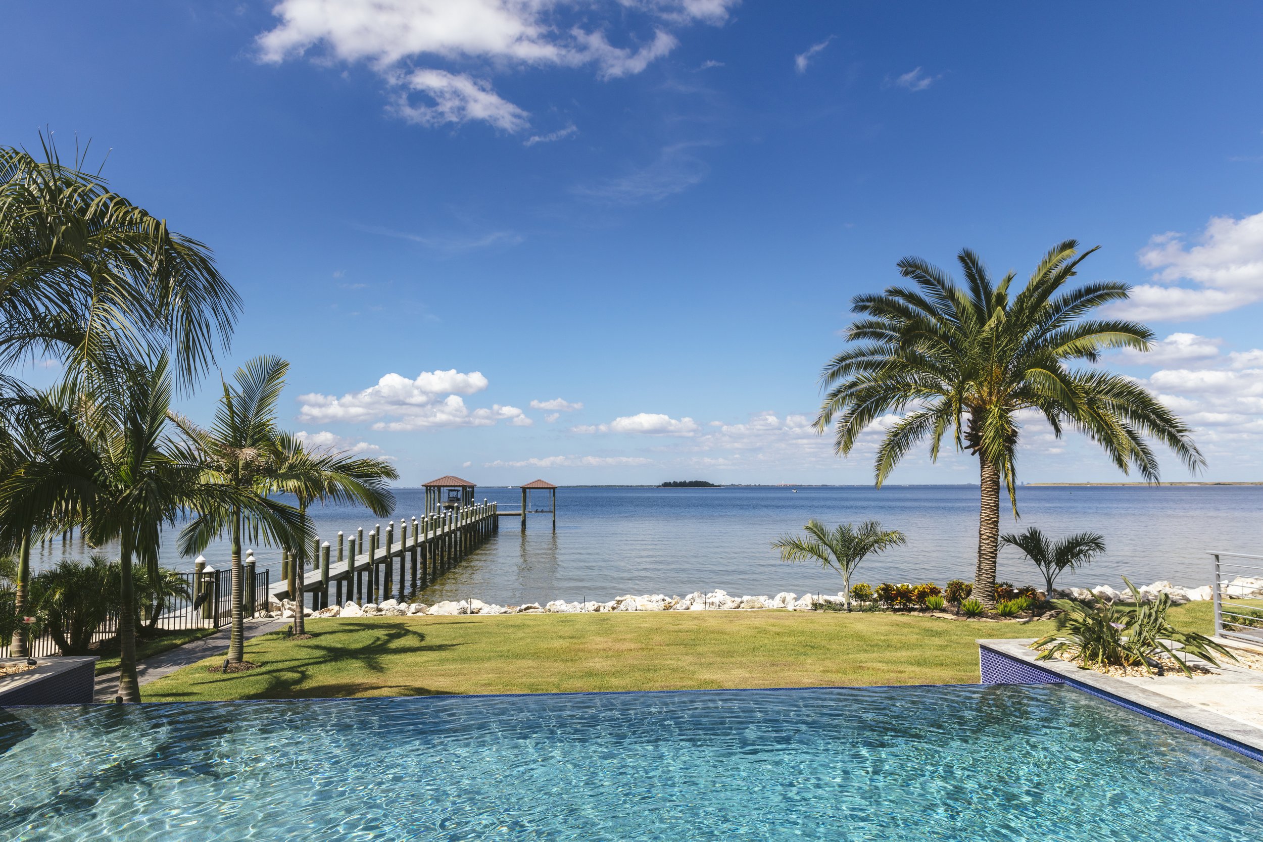 gorgeous pool and seaside views with palm trees, grass, and walk way
