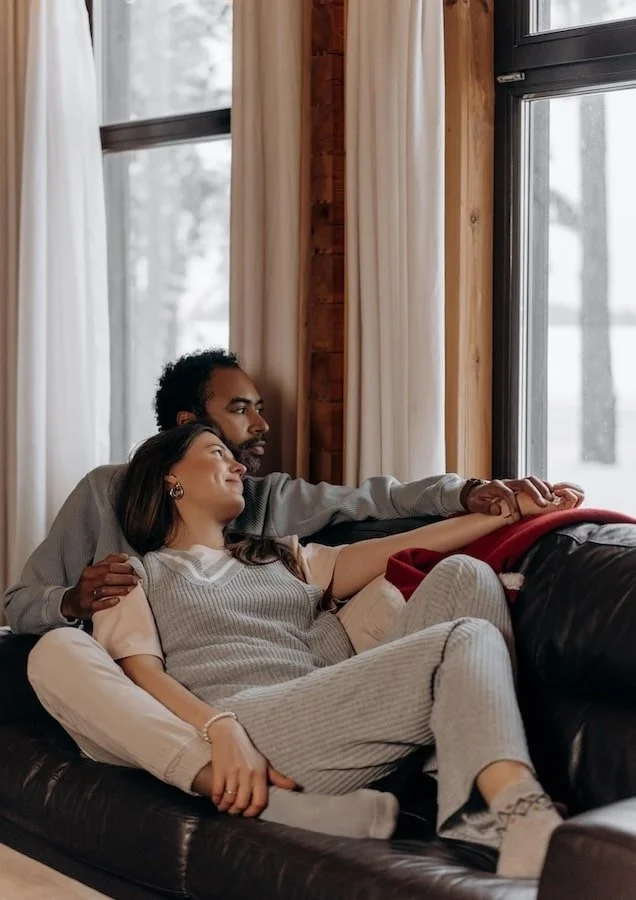 Couple cuddling on the couch while looking out the window.
