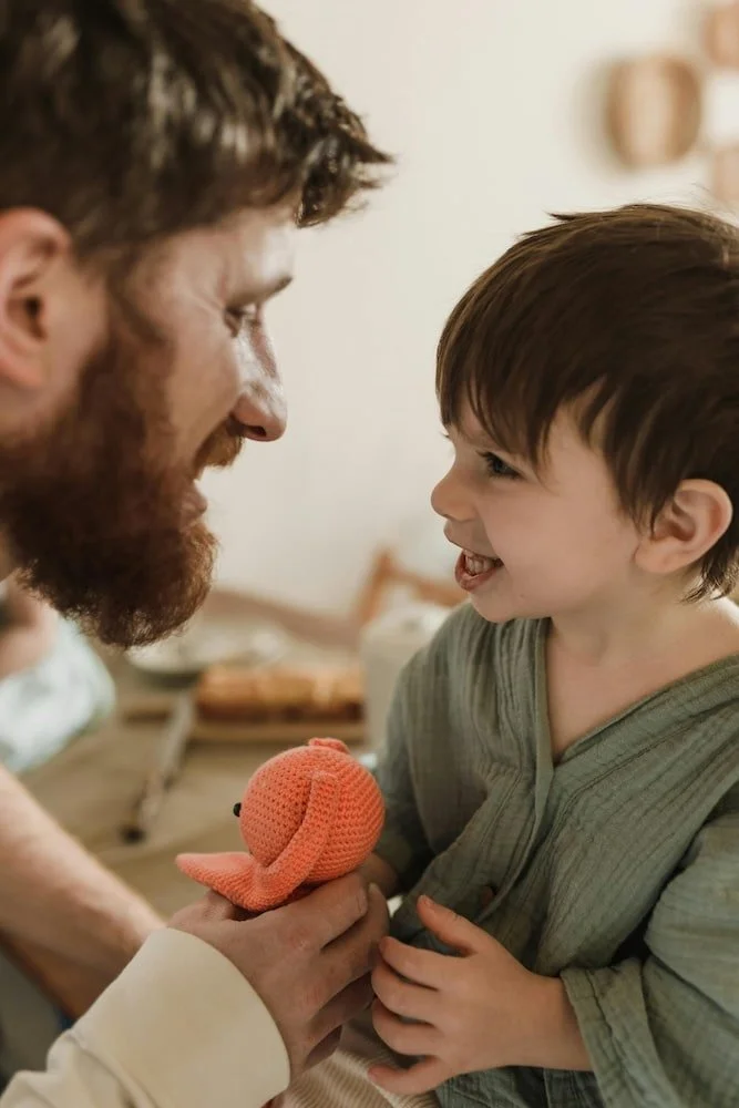 Dad and toddler son smiling at one another