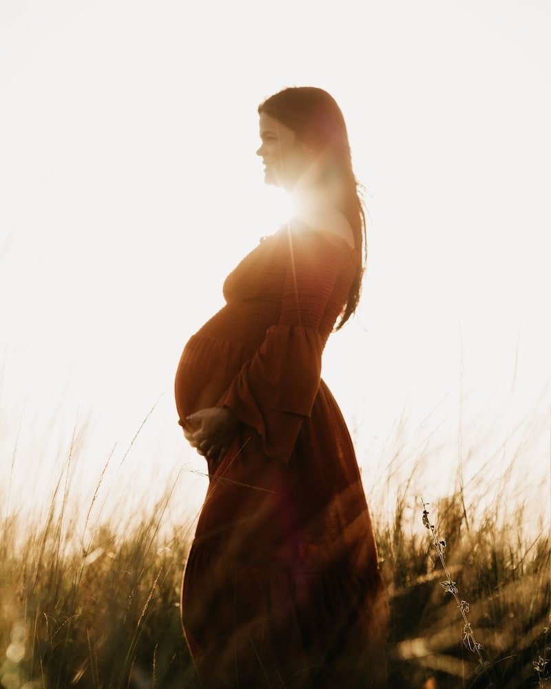 Profile view of pregnant woman holding her belly in a field