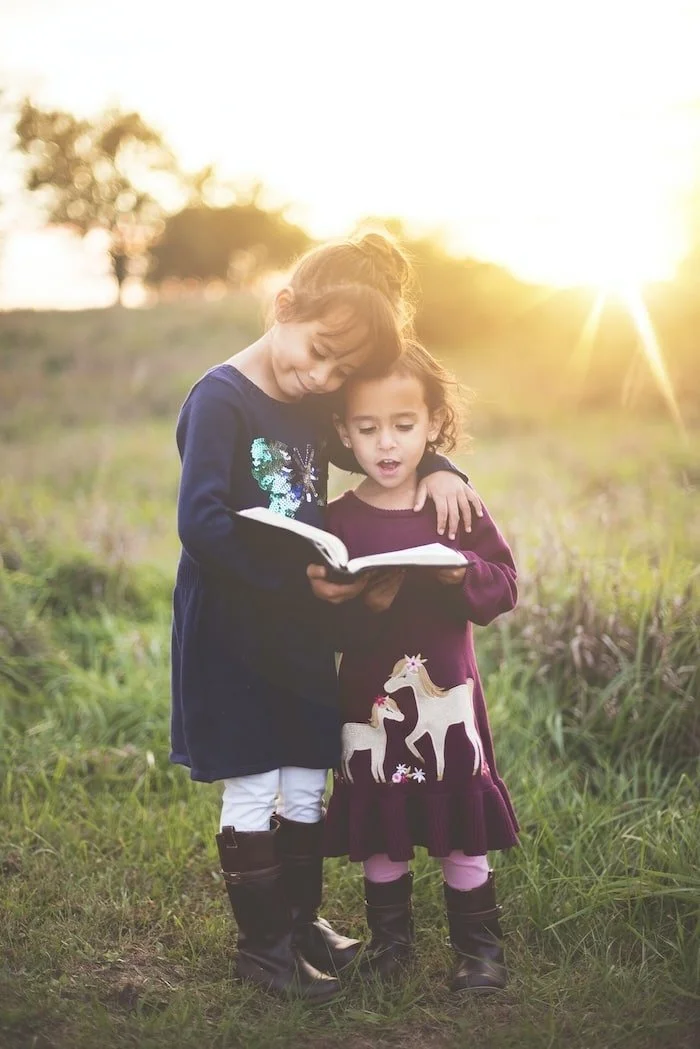 Little sister reading to big sister in a field
