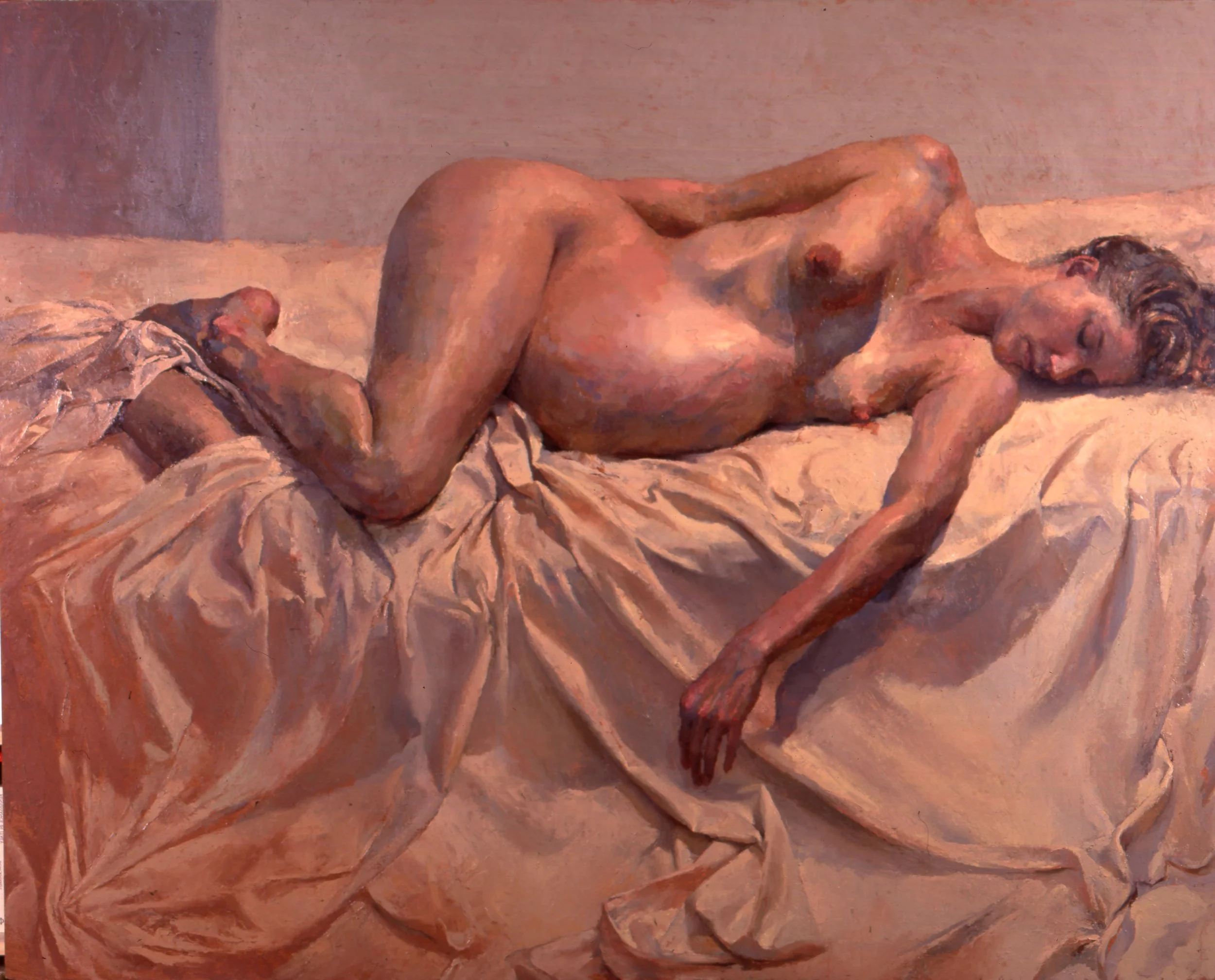 A nude woman lies on her side on a bed with light-colored sheets, resting with her eyes closed and her left arm stretched out on the bed.