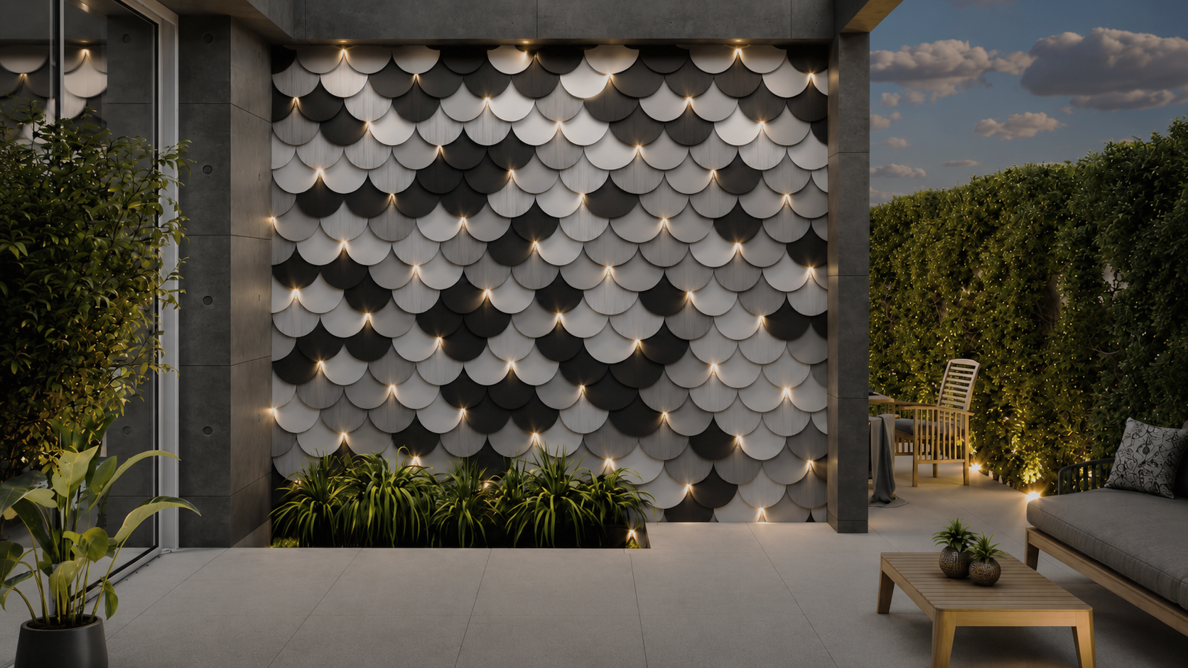 Modern outdoor patio with a decorative wall of black and white scalloped panels, illuminated by built-in lighting. The space features a sofa with pillows, a wooden coffee table with small potted plants, and a dining area with chairs and a table. Green hedges and plants surround the area, and the scene is set during dusk with a partly cloudy sky.