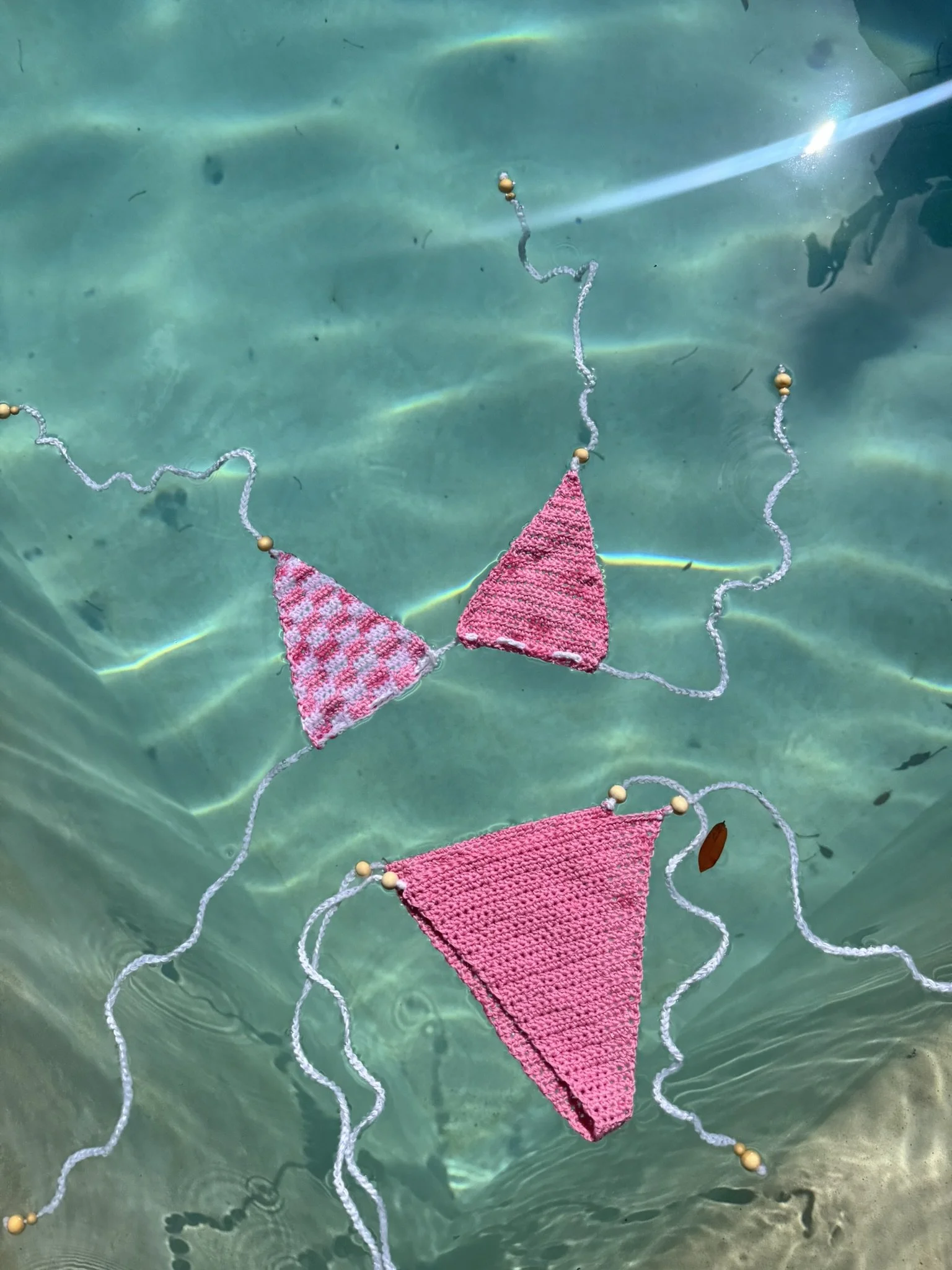 Colorful crocheted swimwear with beads, floating on water.
