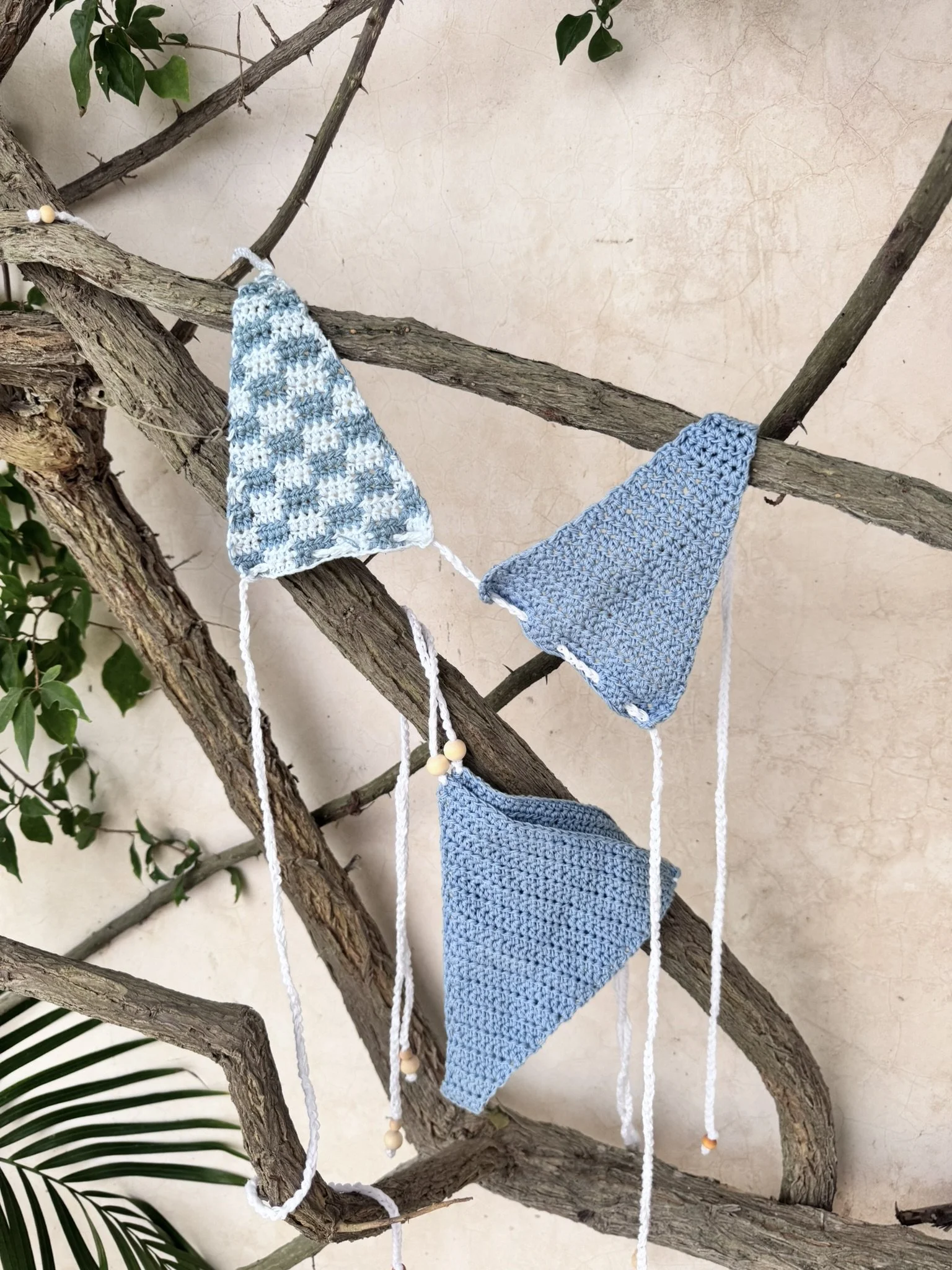 Handmade blue and white crocheted swimwear pieces hanging on a tree branch.