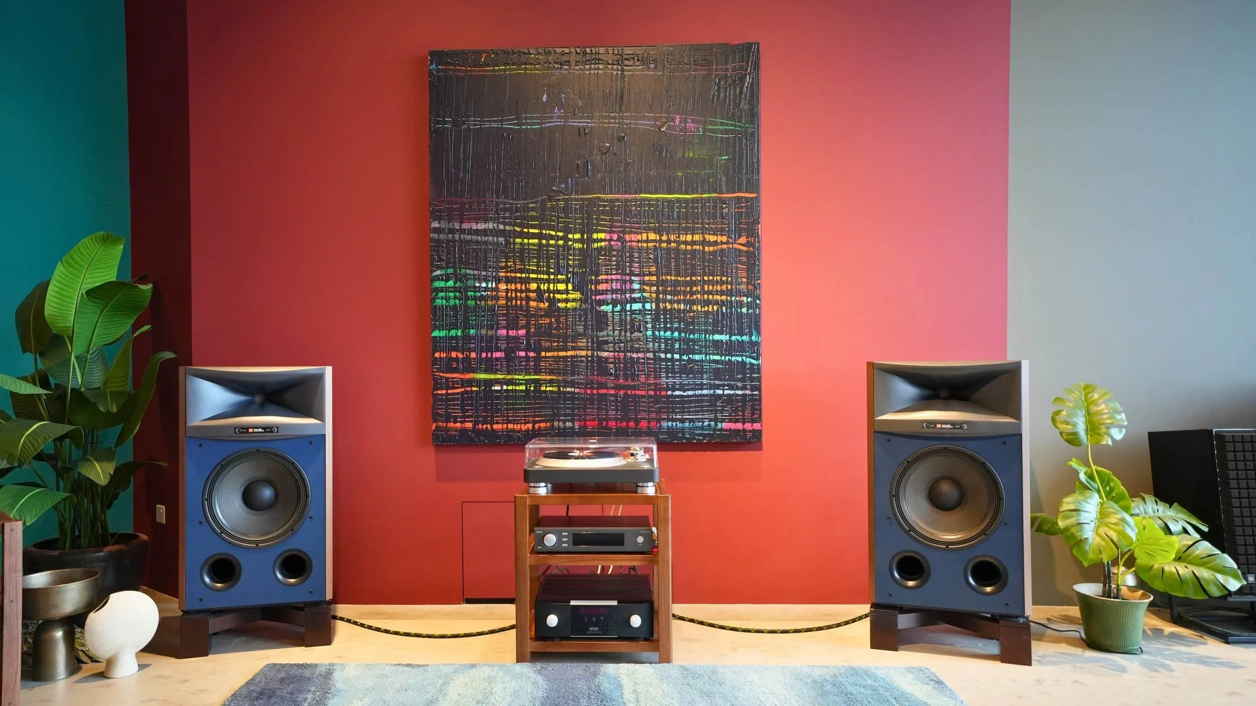 Audio system with Hi-Fi Speakers, a turntable, and a colorful abstract painting on a red wall, surrounded by green houseplants.