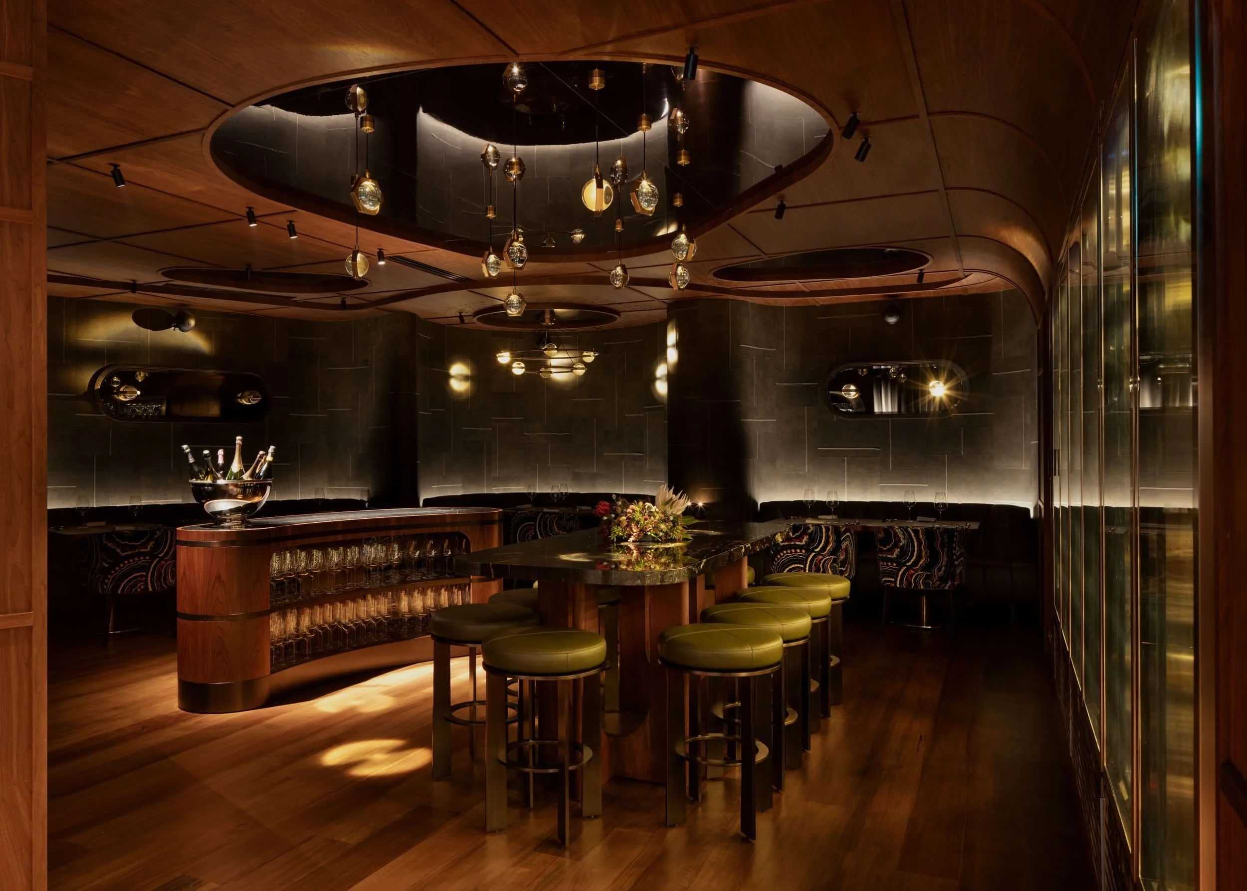 Dimly lit, modern bar with wooden decor and a Restaurant Sound System, offering cozy elegance with round tables and pendant lights.
