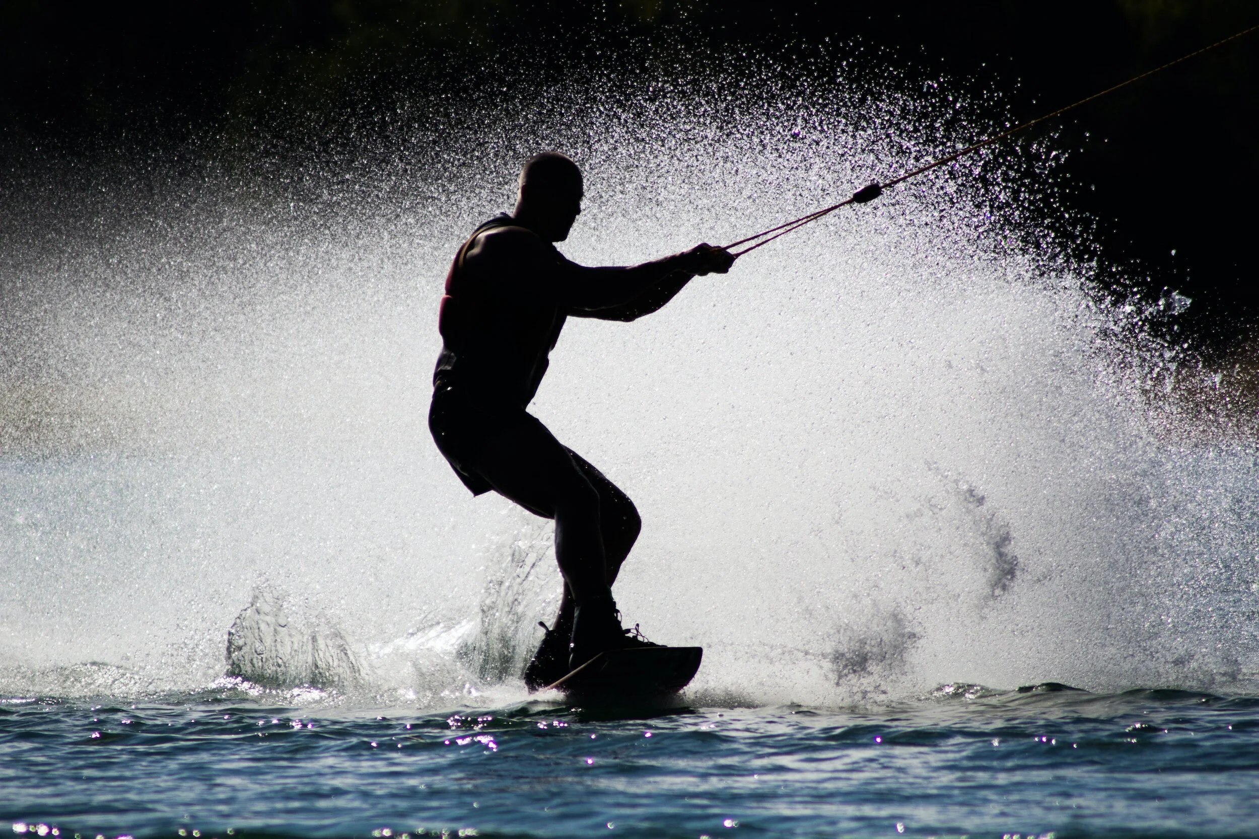 Silhouette of a person wakeboarding back to the boat dock in Christina Lake with spray in the background. One of the many water activities to do while camping at Skands.