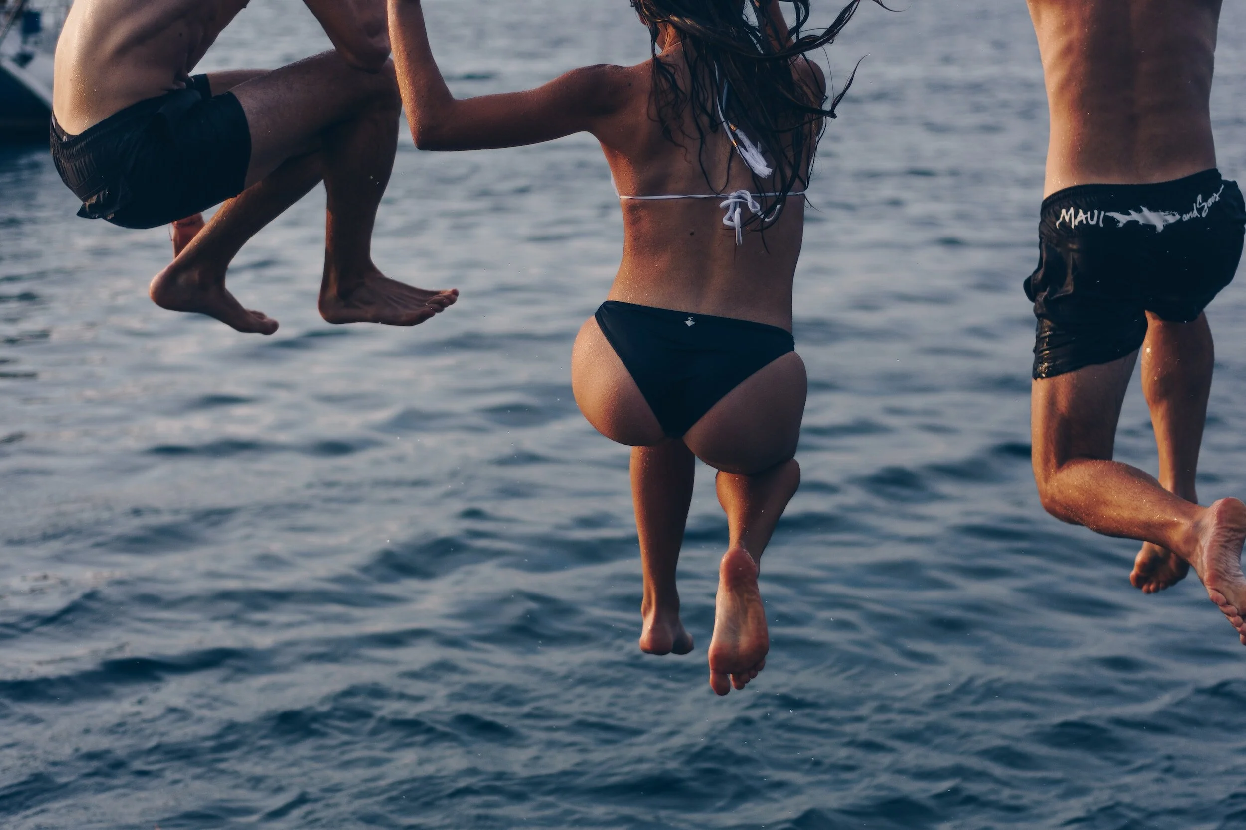 Three teenagers jumping off the dock at the same time, while camping at Skands into Christina Lake.
