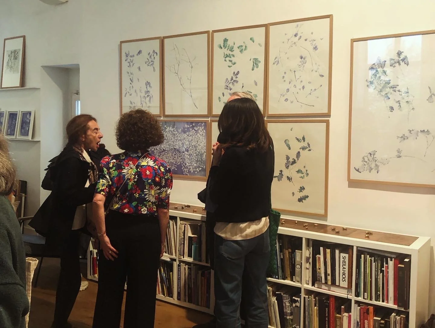 Group of people viewing framed botanical art prints on gallery wall in an art exhibition.