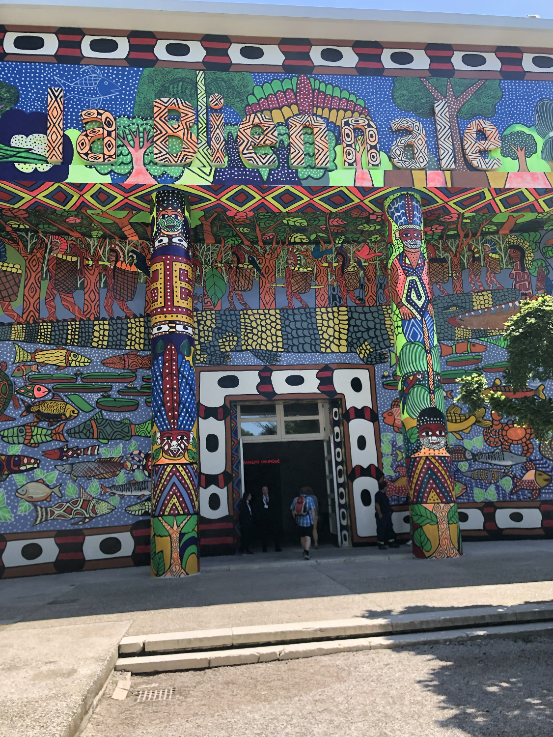 Colorful mural on a building facade with tribal patterns, animals, fish, and the text 'La Biennale' at the top.