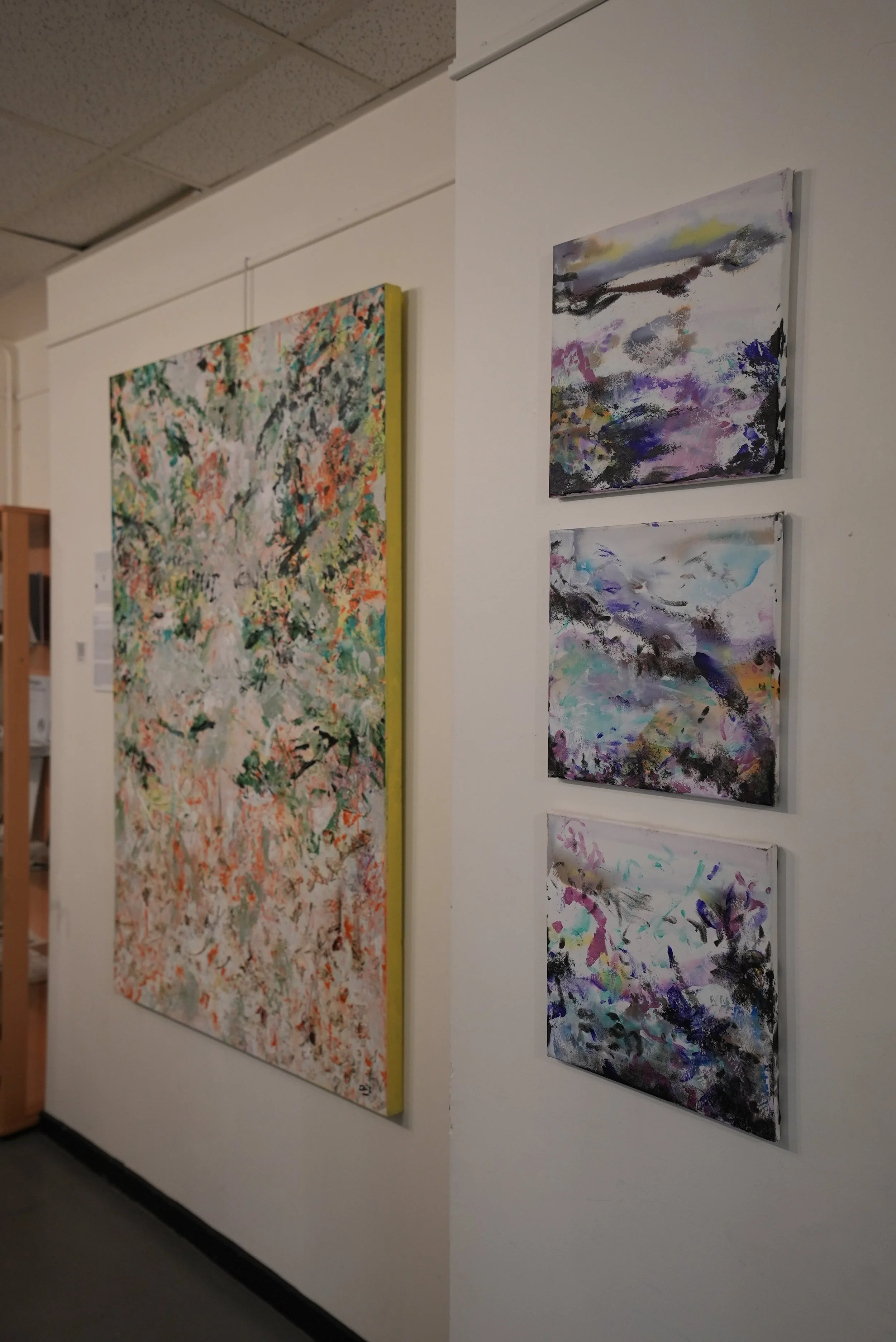 Abstract paintings on white gallery walls, including a large multi-colored work on the left and three smaller, sky-colored paintings on the right.