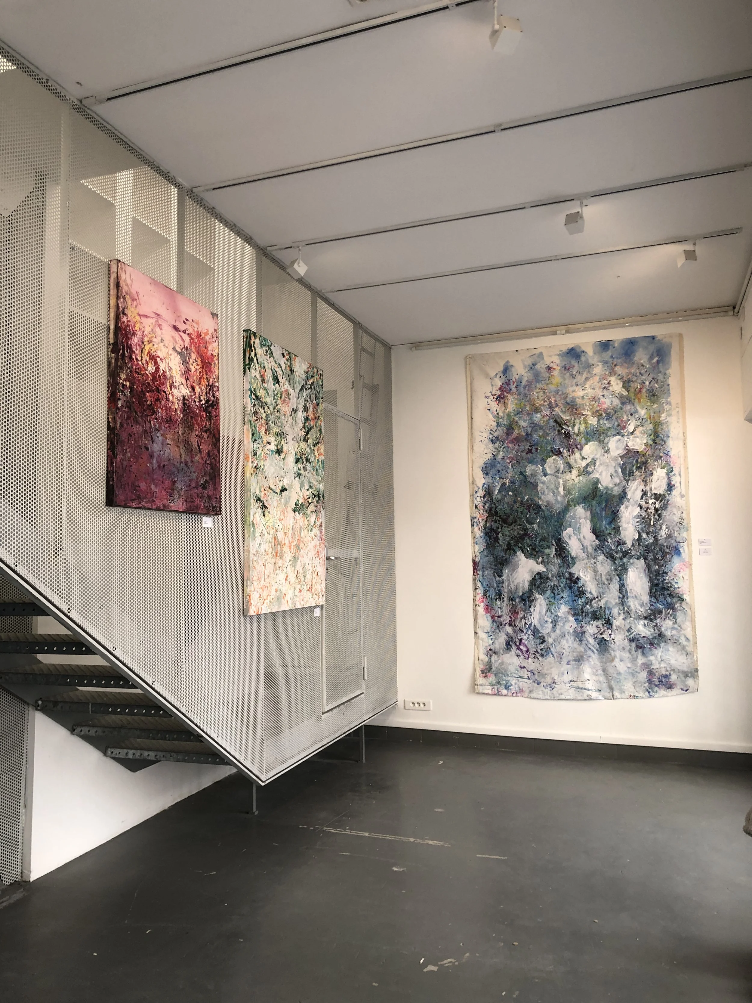 Gallery with three abstract paintings on white and gray walls, featuring colorful, textured brushstrokes. modern art, contemporary art famous artist in paris