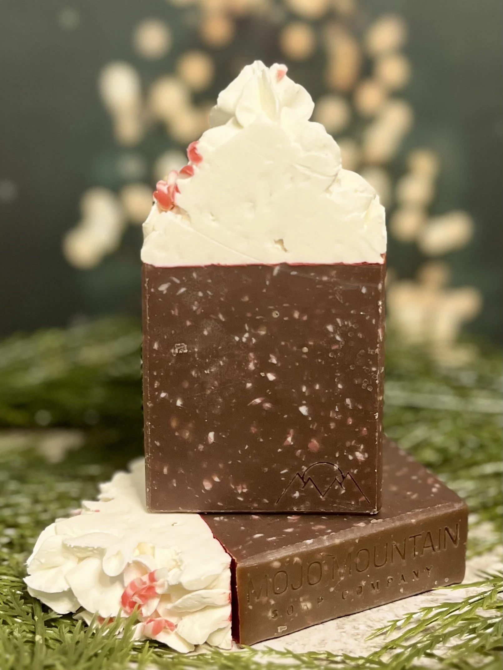 A bar of chocolate with white frosting and pink decorative elements on top, placed on a snowy surface with greenery in the background.